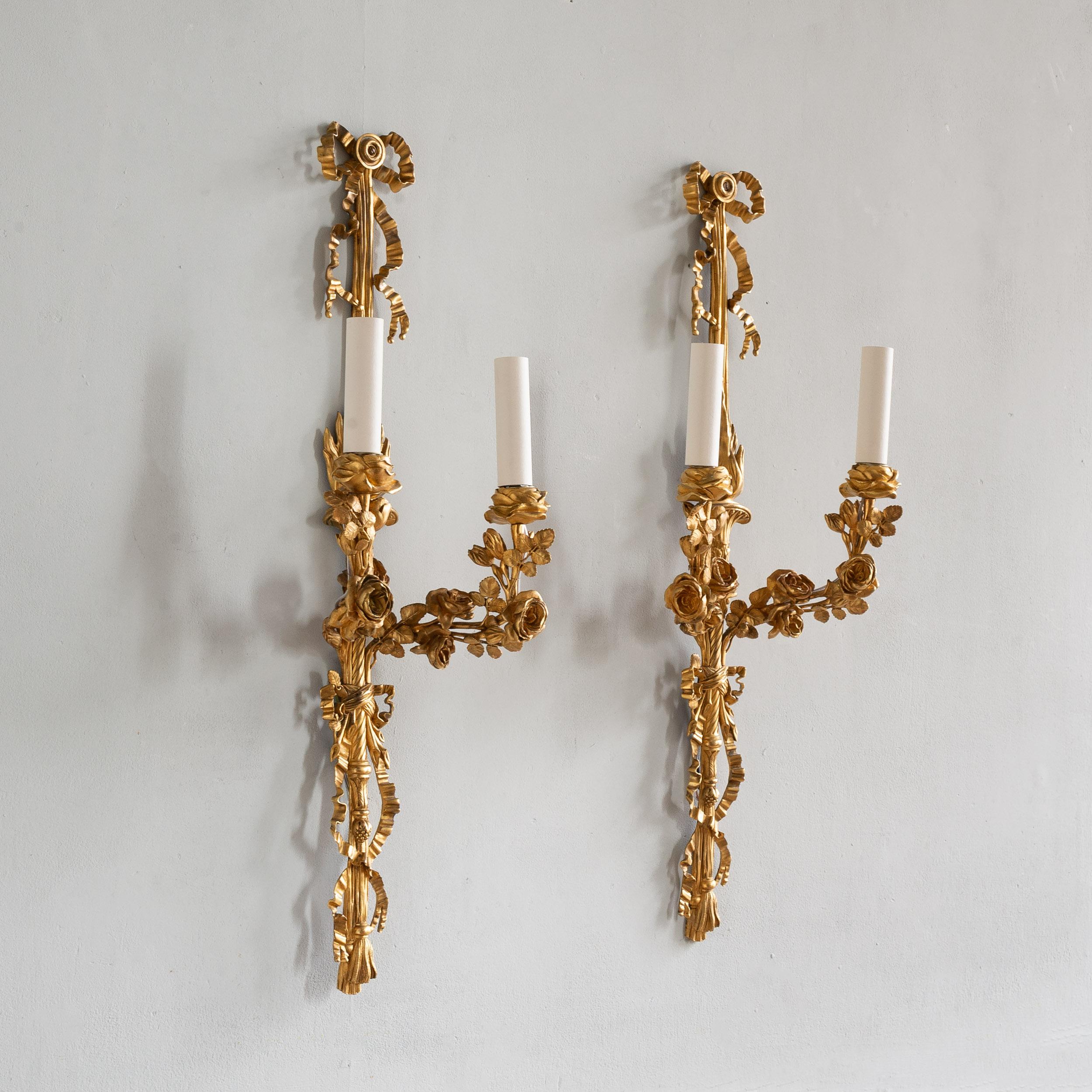 Paire d'appliques murales Louis XVI en bronze doré, XIXe siècle, dans le style du célèbre bronzier français du XVIIIe siècle Lucien François Feuchere. Les corps sont suspendus à des rubans noués, les tiges centrales sont ornées d'urnes flamboyantes