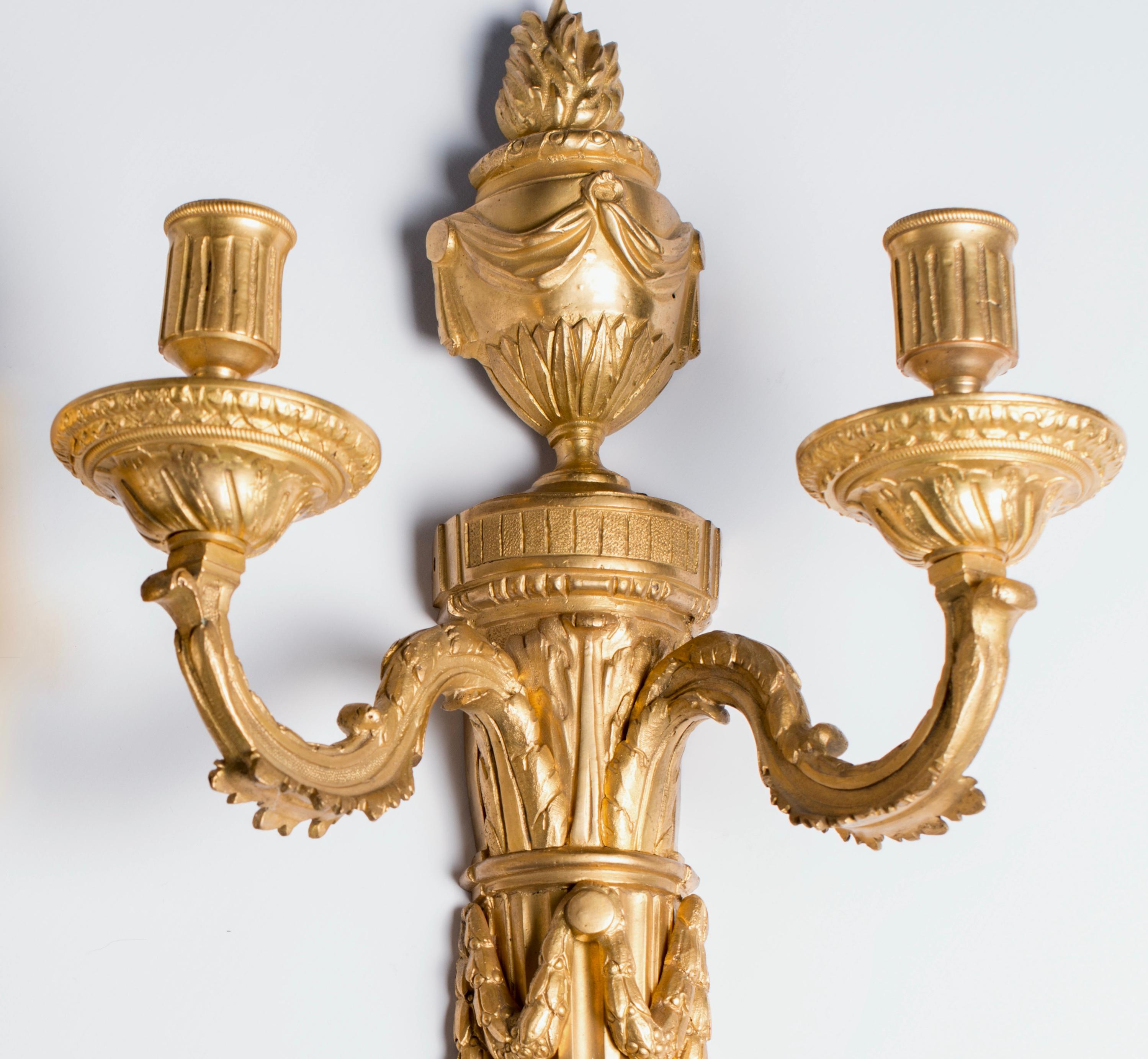 French monumental wall lights are in the neoclassical style and inspired by the Greek and Roman classical period.
The pair of wall lights are nicely casted in bronze and gilded. Each wall light is shown with a stop-fluted backplate surmounted by an