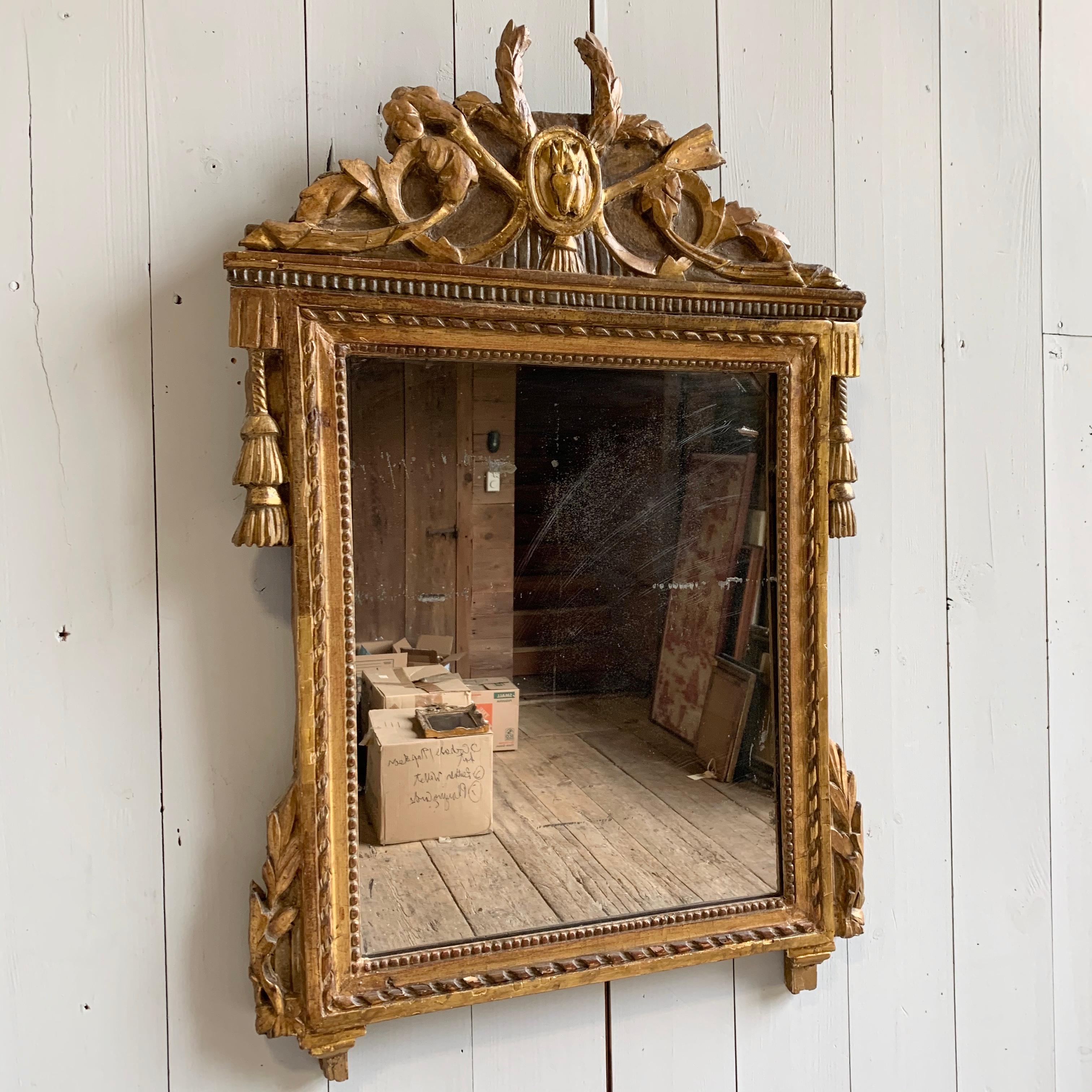A French Louis XVI period giltwood wall mirror with upper crest and other carved decoration including tassels, garlands, etc. Original mercury plate glass mirror, circa 1790.