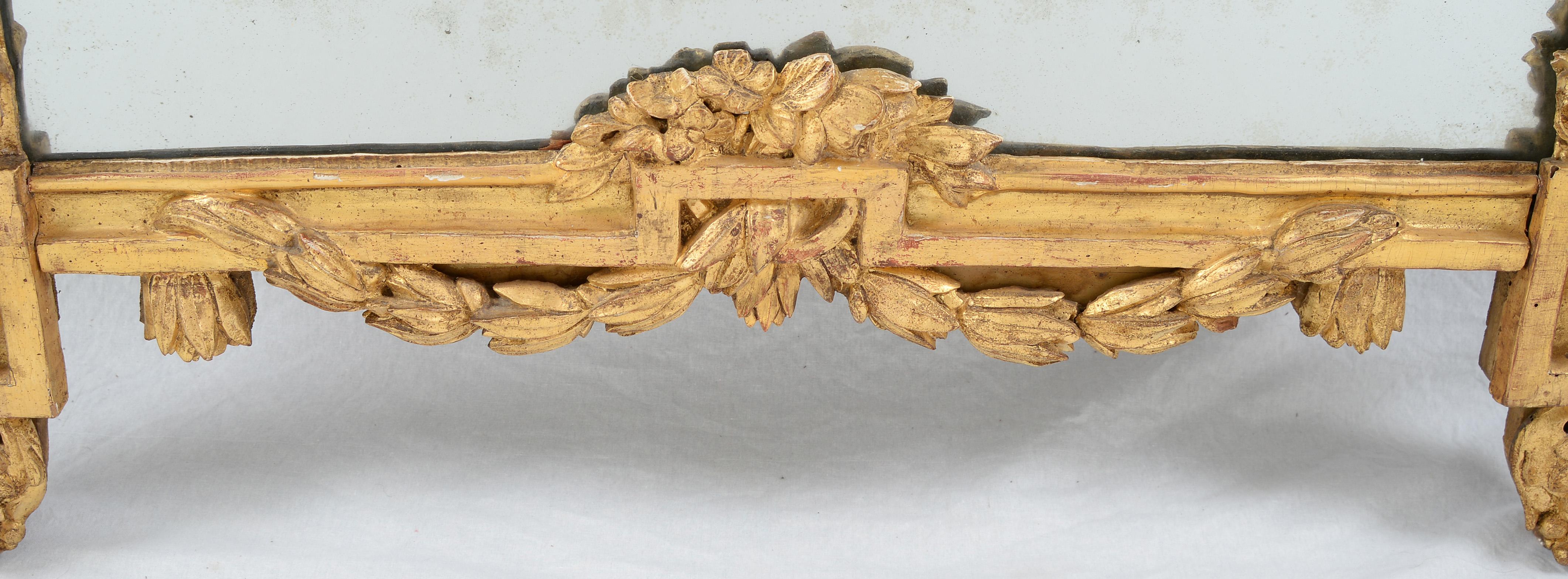 Miroir en bois doré de style Louis XVI dans le goût grec, de forme rectangulaire surmonté d'une urne en cercle et suspendu par une guirlande de feuillage en ruban, enveloppant partiellement chaque côté derrière les coins supérieurs.  

Avec sa crête