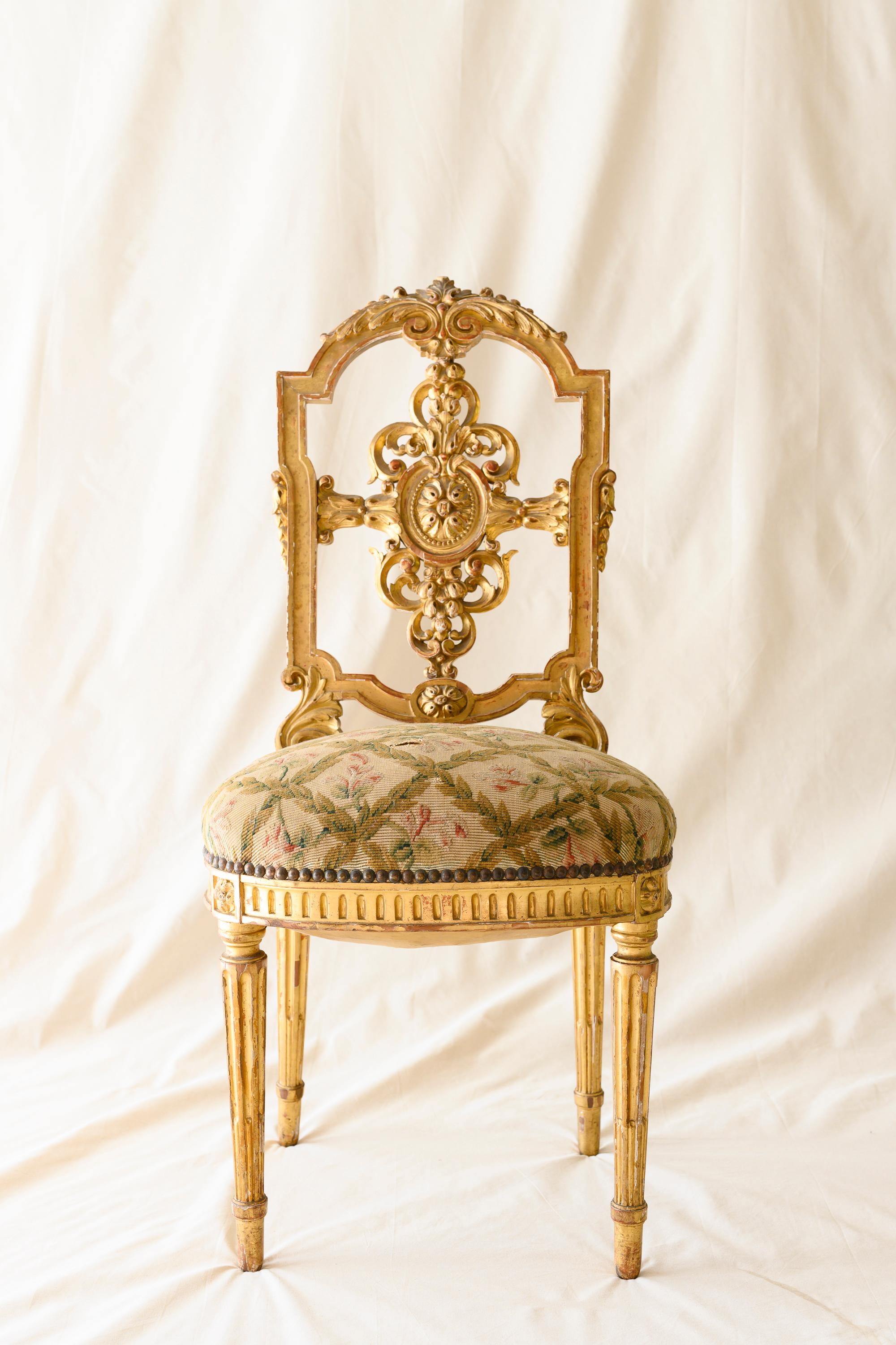 Suite of four Louis XVI giltwood chairs in the style of Versailles. Each boasts a delicately carved splat with a rosette medallion surrounded by intricate foliage on a shield- shaped backrest, with a curved molded top rail carved with two resting