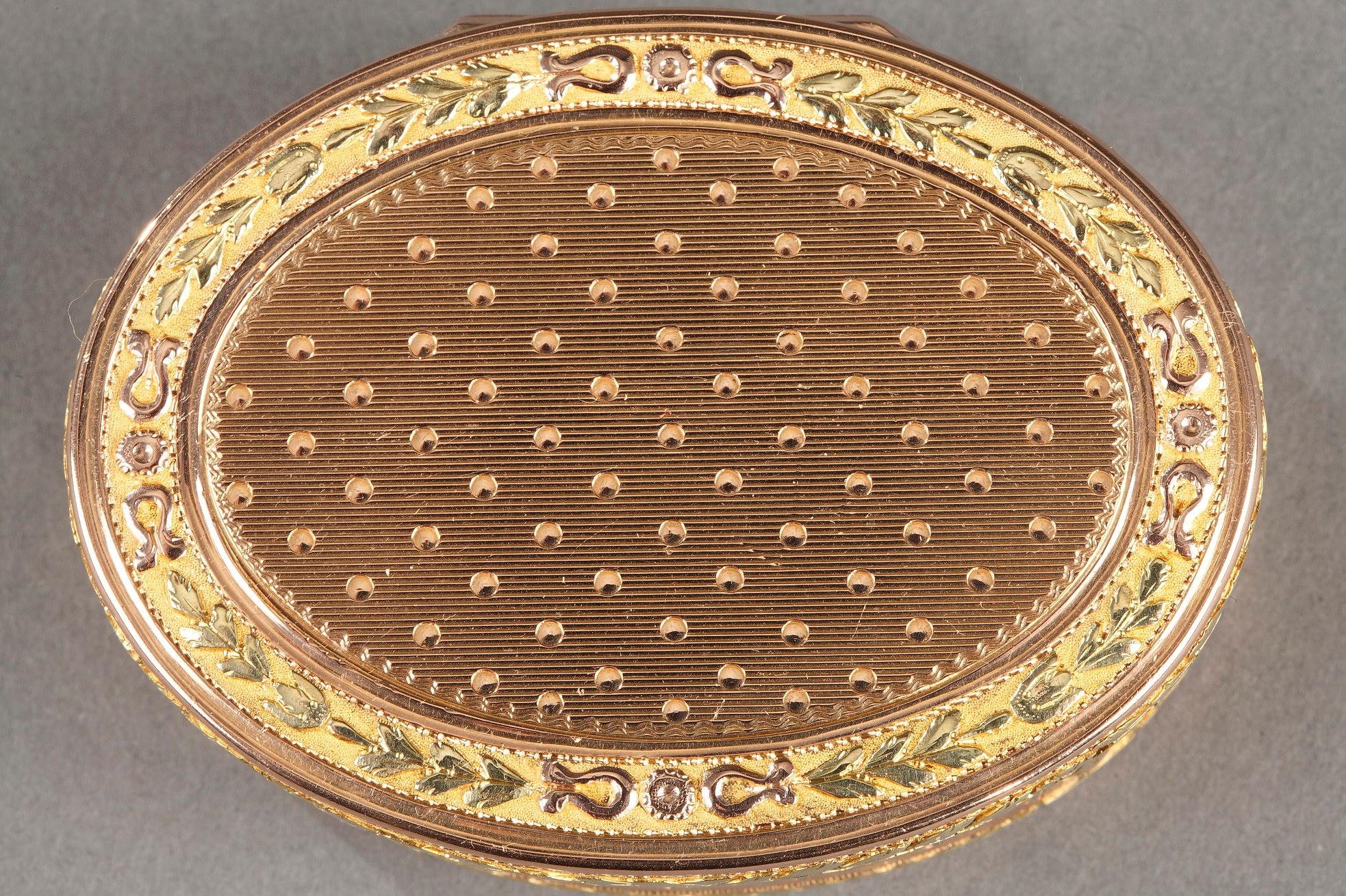 Oval box or snuffbox in gold of several tones. The snuffbox is adorned with a guilloche pattern with parallel stripes and dots on the lid, side and ground. The border is decorated with a stylized laurel wreath frieze on amati background. The box has