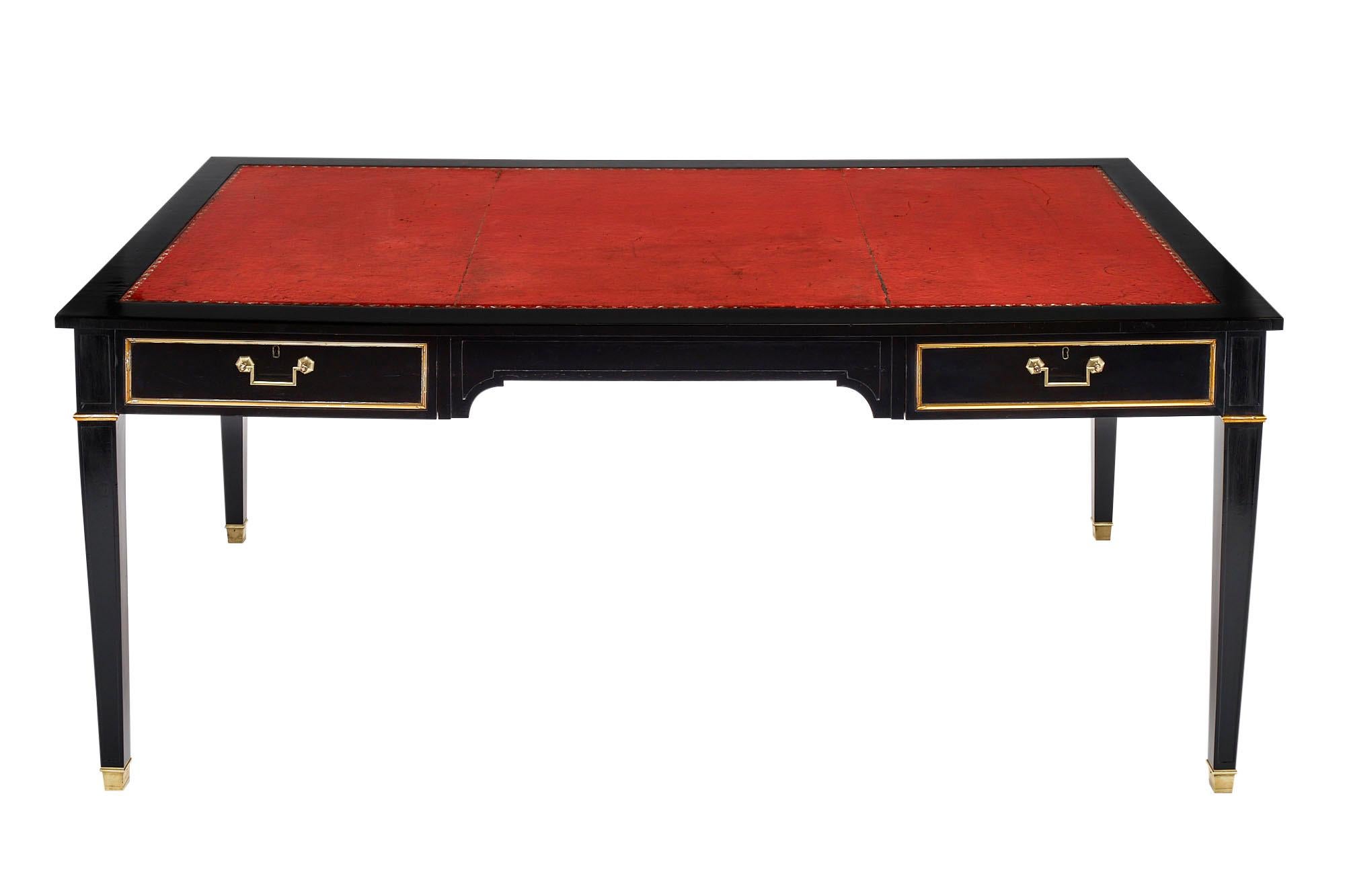 Louis XVI grand antique desk made of mahogany that has been ebonized and finished with a museum quality French polish. There are two dovetailed drawers and beautiful gilt trim throughout. We love the brass hardware and squared, tapered legs. The red