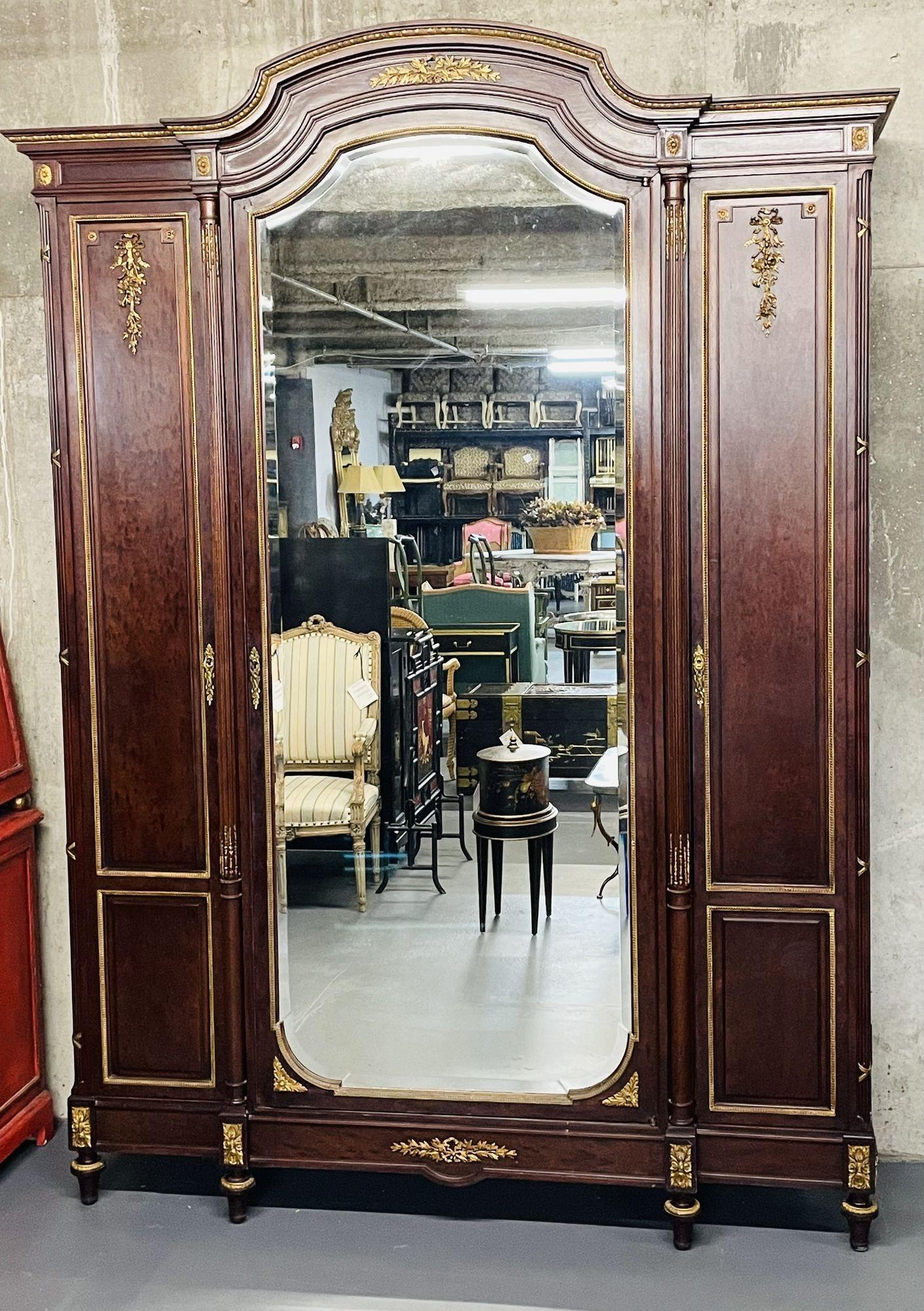 Louis XVI Mahogany Armoire by Mercier Frères. Wardrobe, Linen Press for Bedroom. 
 
A Stunning Dore Bronze Triple door Armoire having a large center Beveled Mirror Door flanked by a pair of smaller doors. the case of a fine mahogany having all