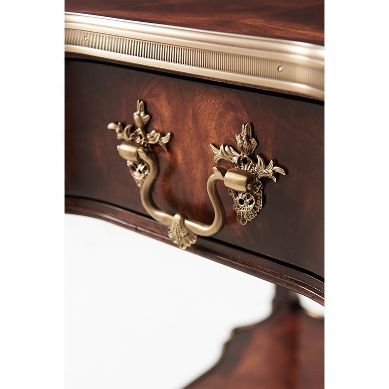A Louis XVI style mahogany veneer end table, the serpentine square brass bound top above a shaped frieze drawer with finely cast brass Rocaille handle, on square tapering and fluted legs applied with roundels and joined by a serpentine brass bound