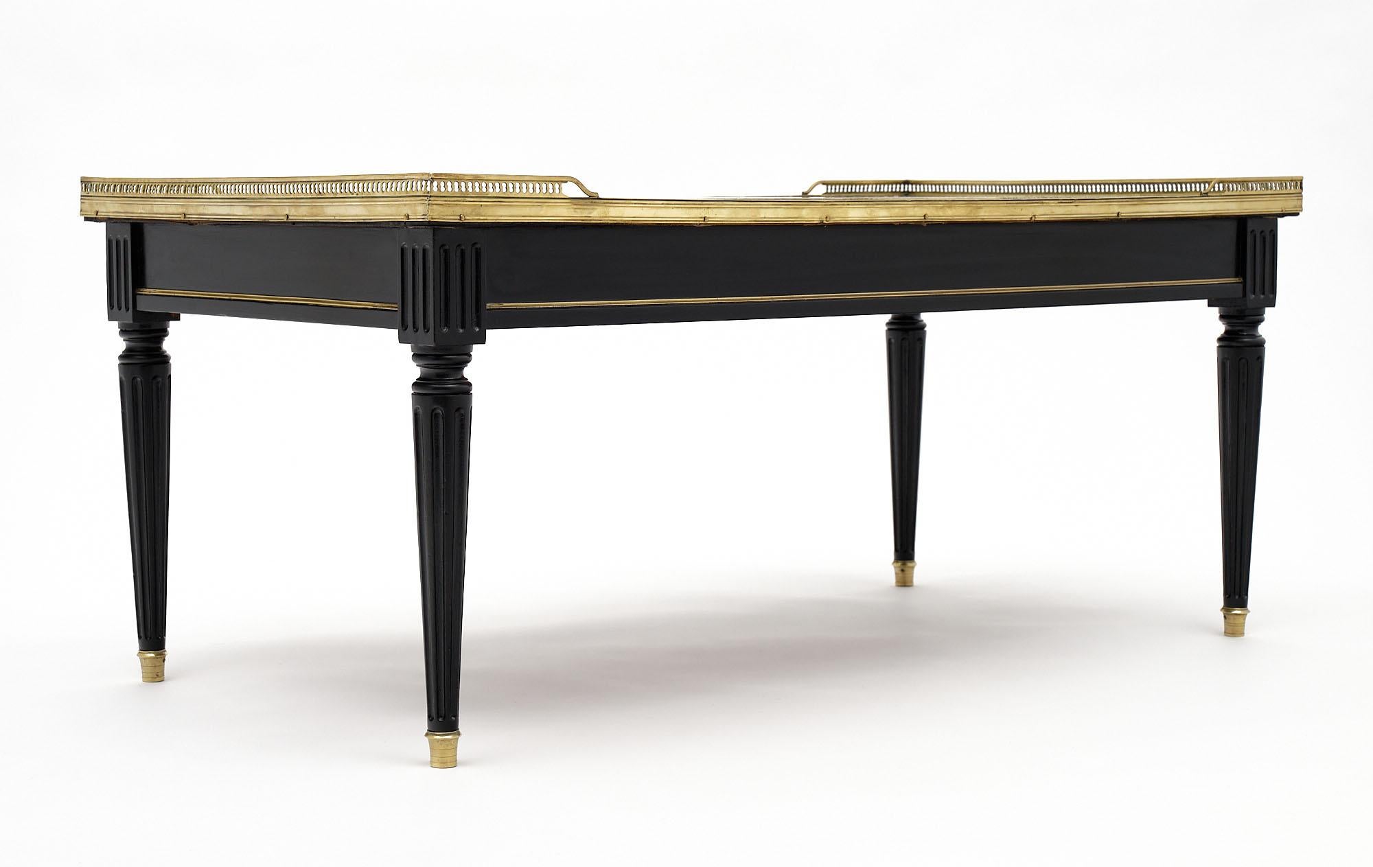 Louis XVI Maison Jansen coffee table made of ebonized mahogany with a Michelangelo Carrara marble top. The marble is surrounded with an opened gilt brass gallery and is supported with fluted legs. We love the brass details and beautiful Classic