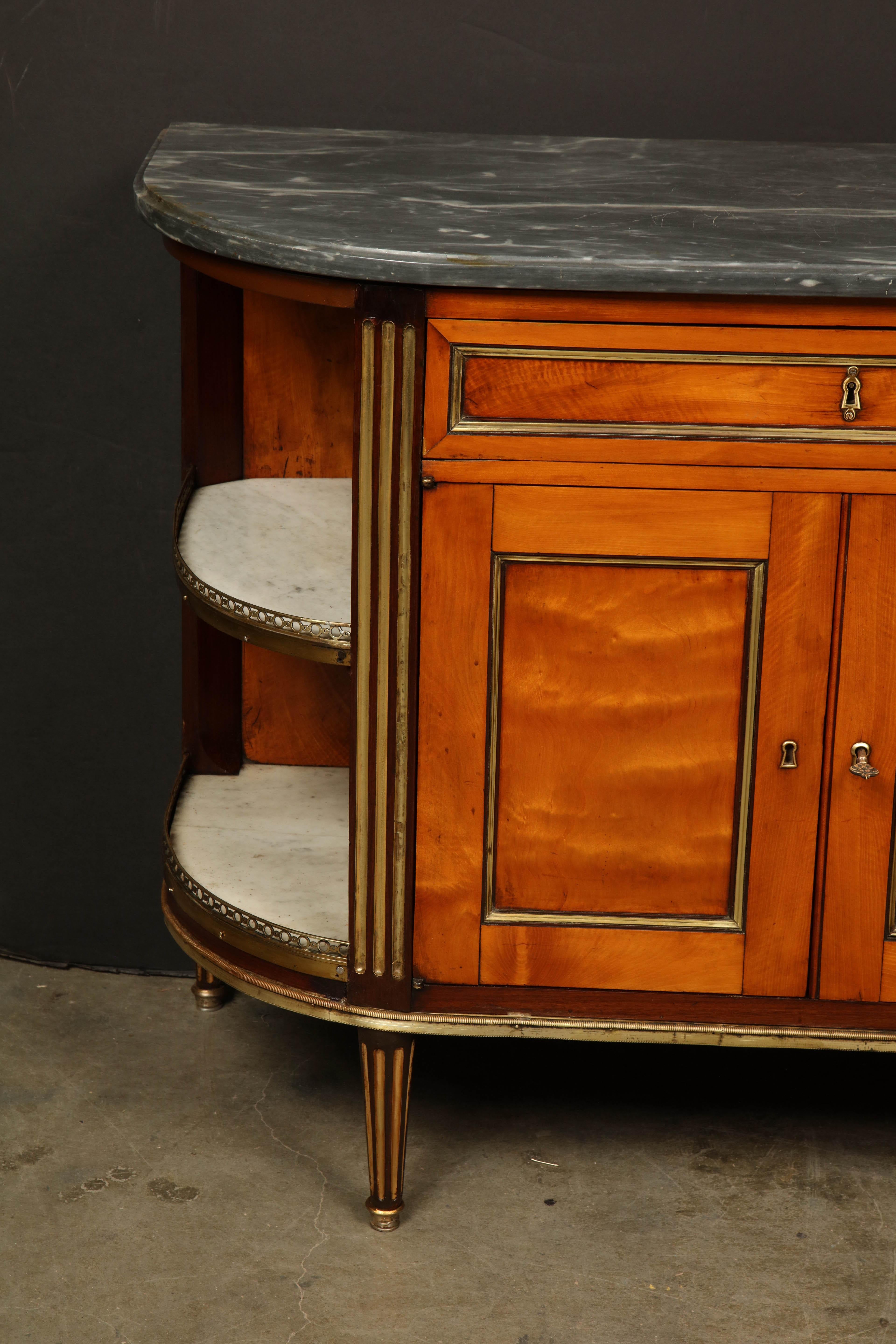 An unusual French Louis XVI marble-top satinwood 'D' form cabinet with a fold-down desk, above a two-door cabinet and four open shelves on tapered and fluted legs.