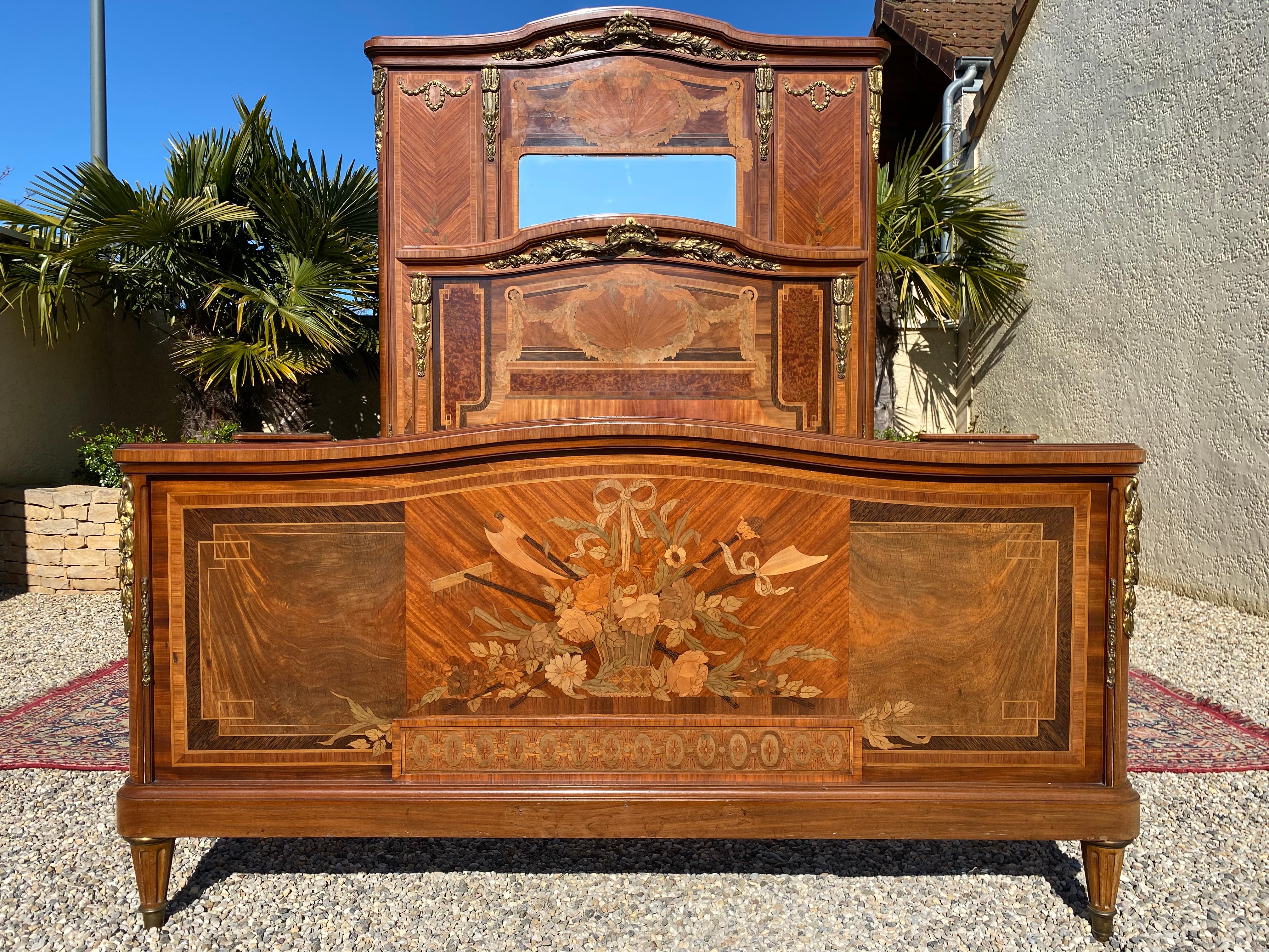 Sumptuous bedroom set of very high quality. This bedroom is composed of a bed, a wardrobe, a mirror and two bedside tables. The whole is in marquetry composed of different woods and the whole is decorated with chiseled gilded bronzes.
The bed is
