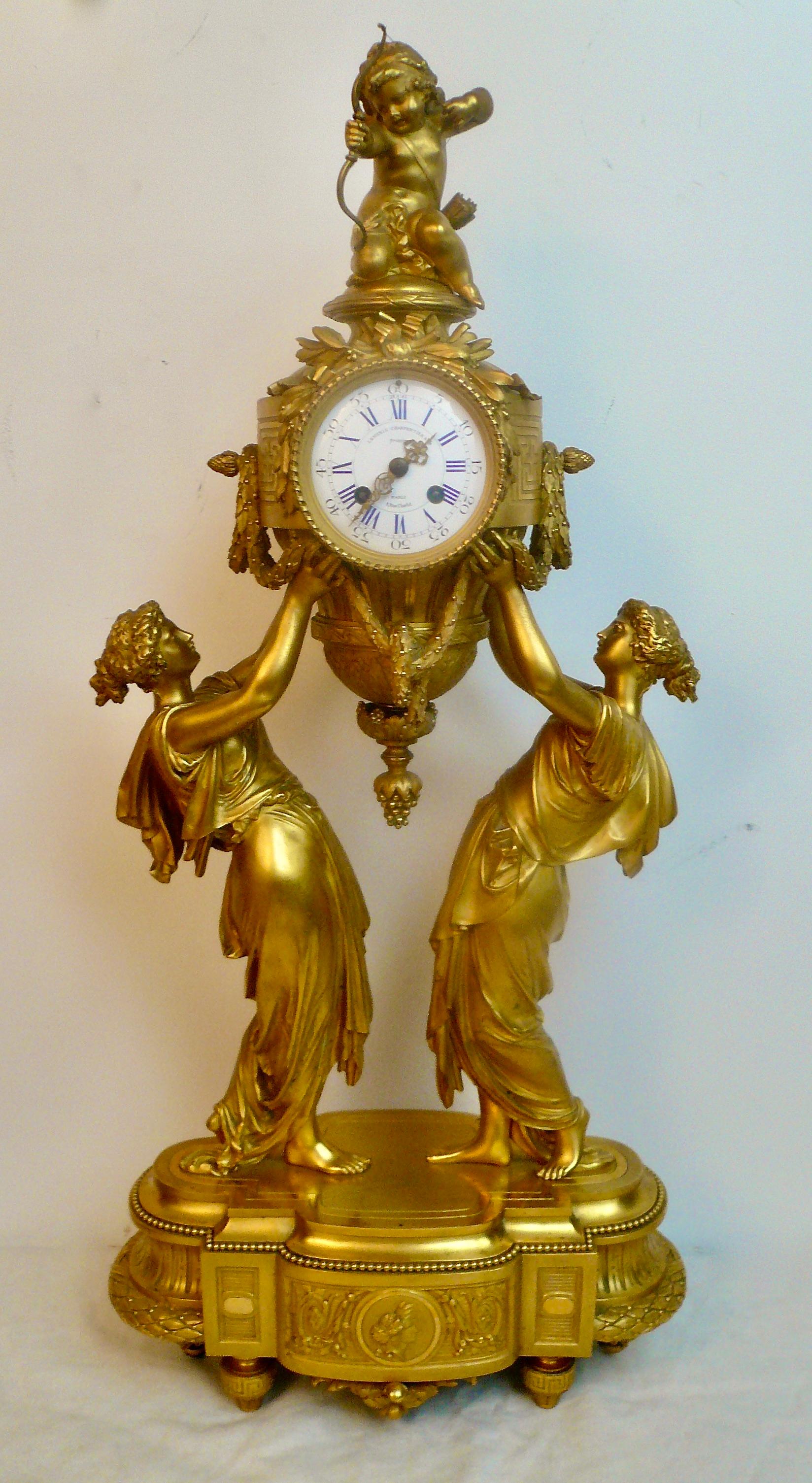 This large and impressive clock is by the renown French Bronzier Lemerle Charpentier & Cie.  It features Classical maidens holding a large urn form case surmounted by Cupid with his bow.  The case is decorated with Classical motifs including