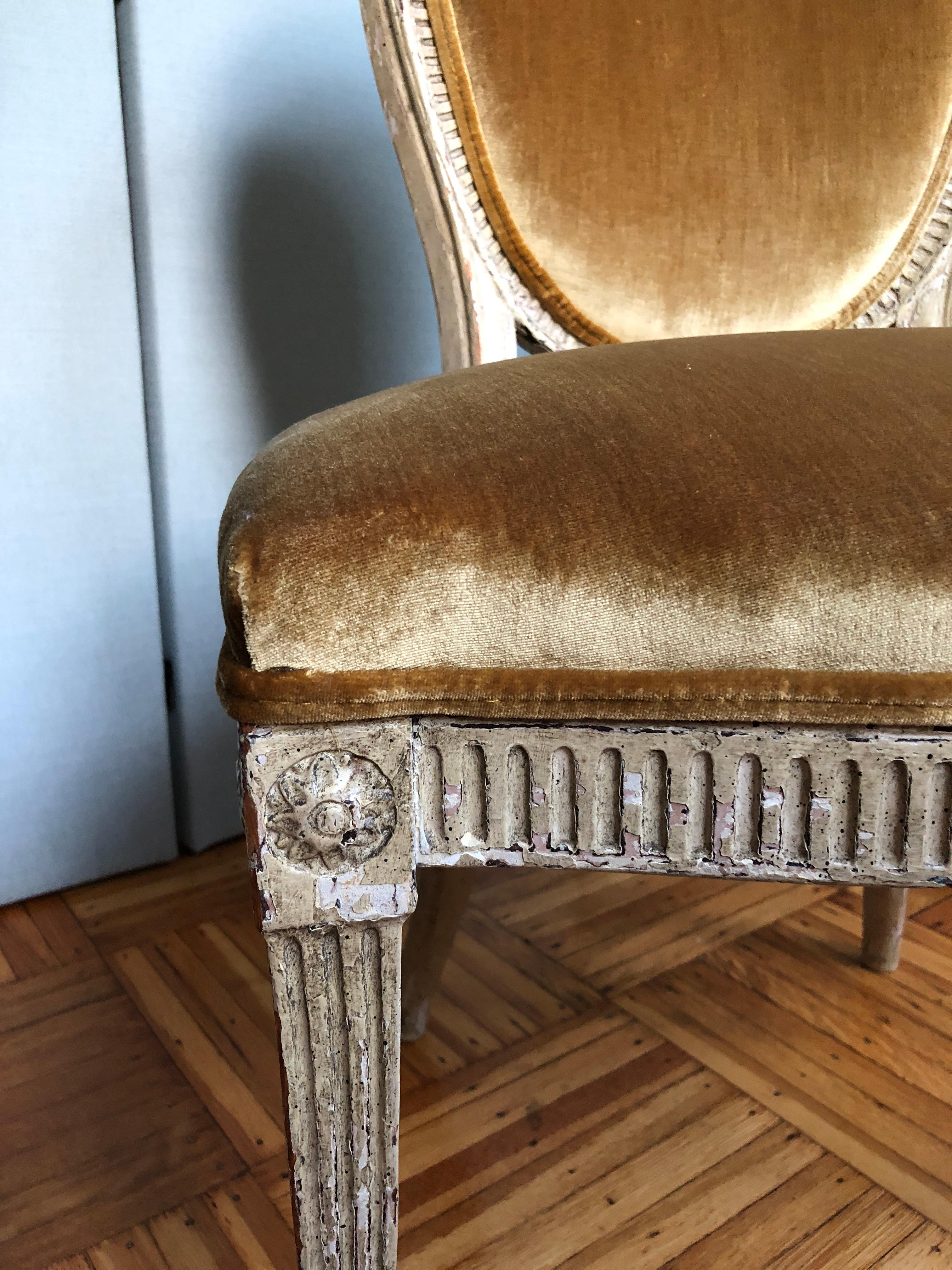 Showroom antique condition with patina on velvet and frame. Year unknown, though irregular carvings and layers of paint suggest handcrafting and antique age. Fluted carved legs with rosettes. Very comfortable curved back support. Reinforced for