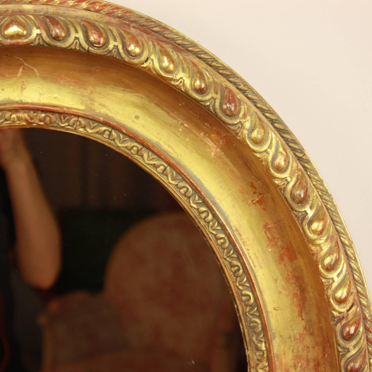 A Louis XVI oval giltwood wall mirror featuring a finely carved band of gadrooning of convex shape. The paisley-like motif is followed by a concave band and a more detailed foliate band. Water gilding of polished and matte quality with some bleeding