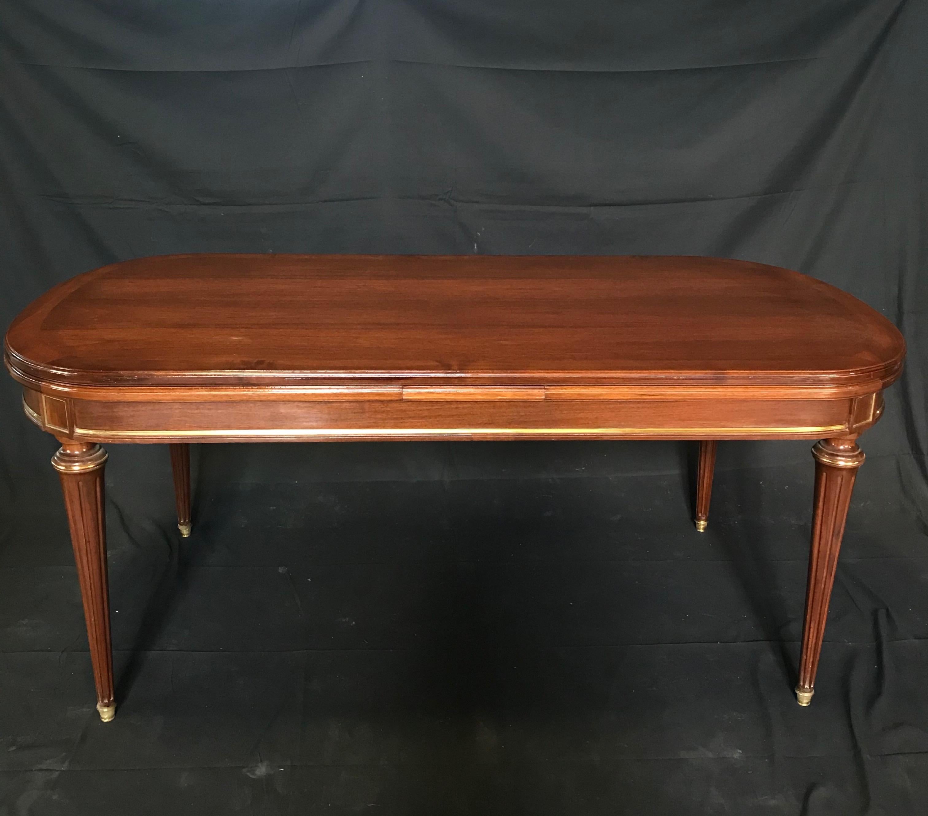 Versatile Louis XVI style oval inlaid banded fruitwood dining table with lacquered finish, bronze banding and two leaves to make it a roomy total length of 9.5 feet. The table has fine details such as gold corner squares, turned fluted legs with