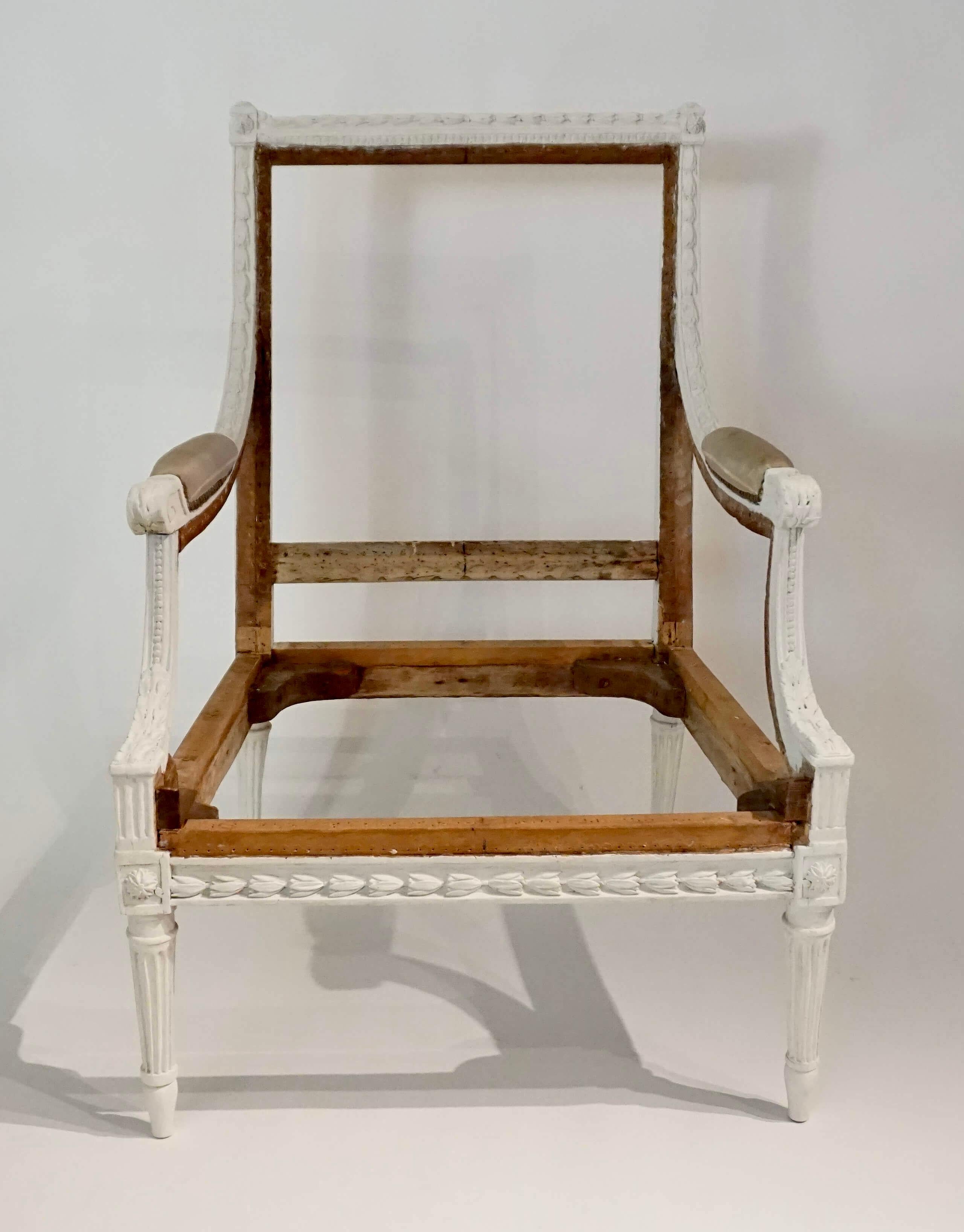 French circa 1780 Louis XVI Bergère à la Reine having painted carved wood frame with allover bellflower motifs on arms, rails, and stiles; the rectangular back issuing sloping padded arms atop sloping arm supports with bead, flute, and acanthus