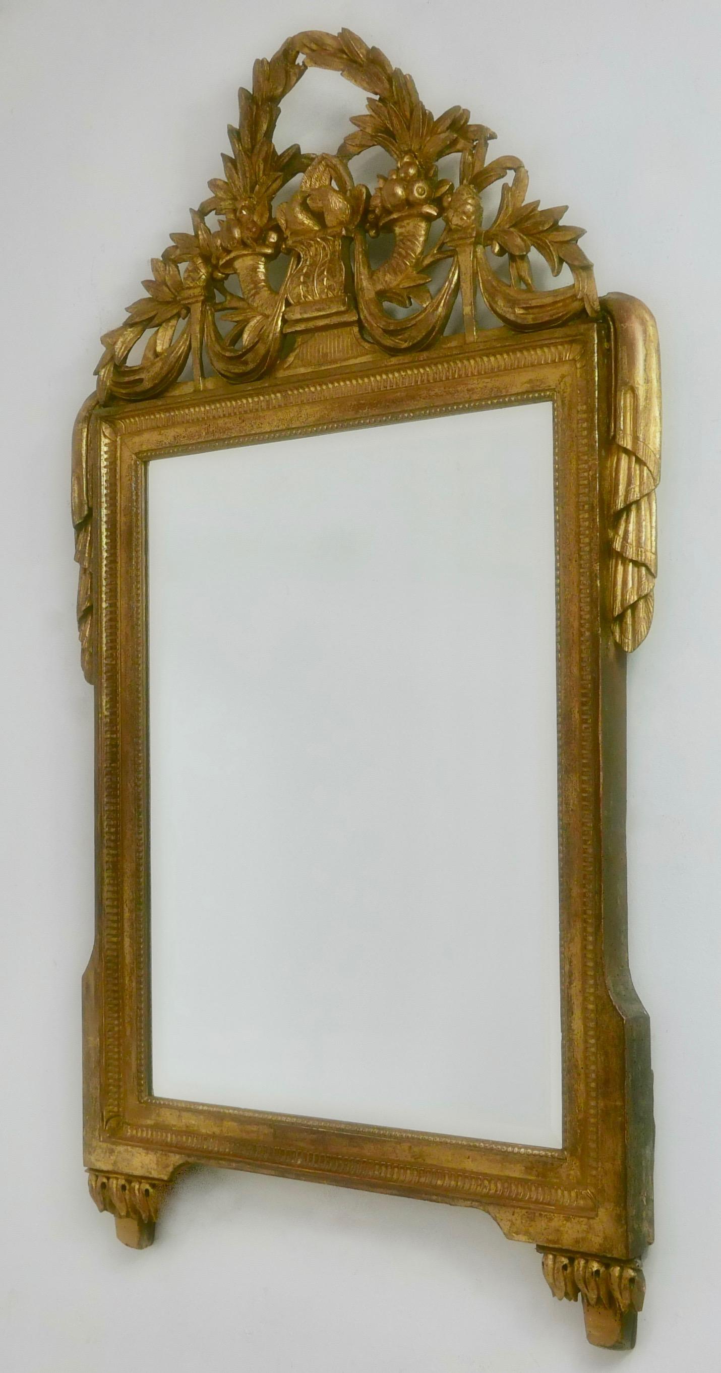 Un beau et bien proportionné miroir Louis XVI encadré de bois sculpté et doré, ayant sa dorure originale qui est magnifiquement vieillie. La couronne incurvée et percée, sculptée de façon complexe, comporte une couronne de laurier, des cornes