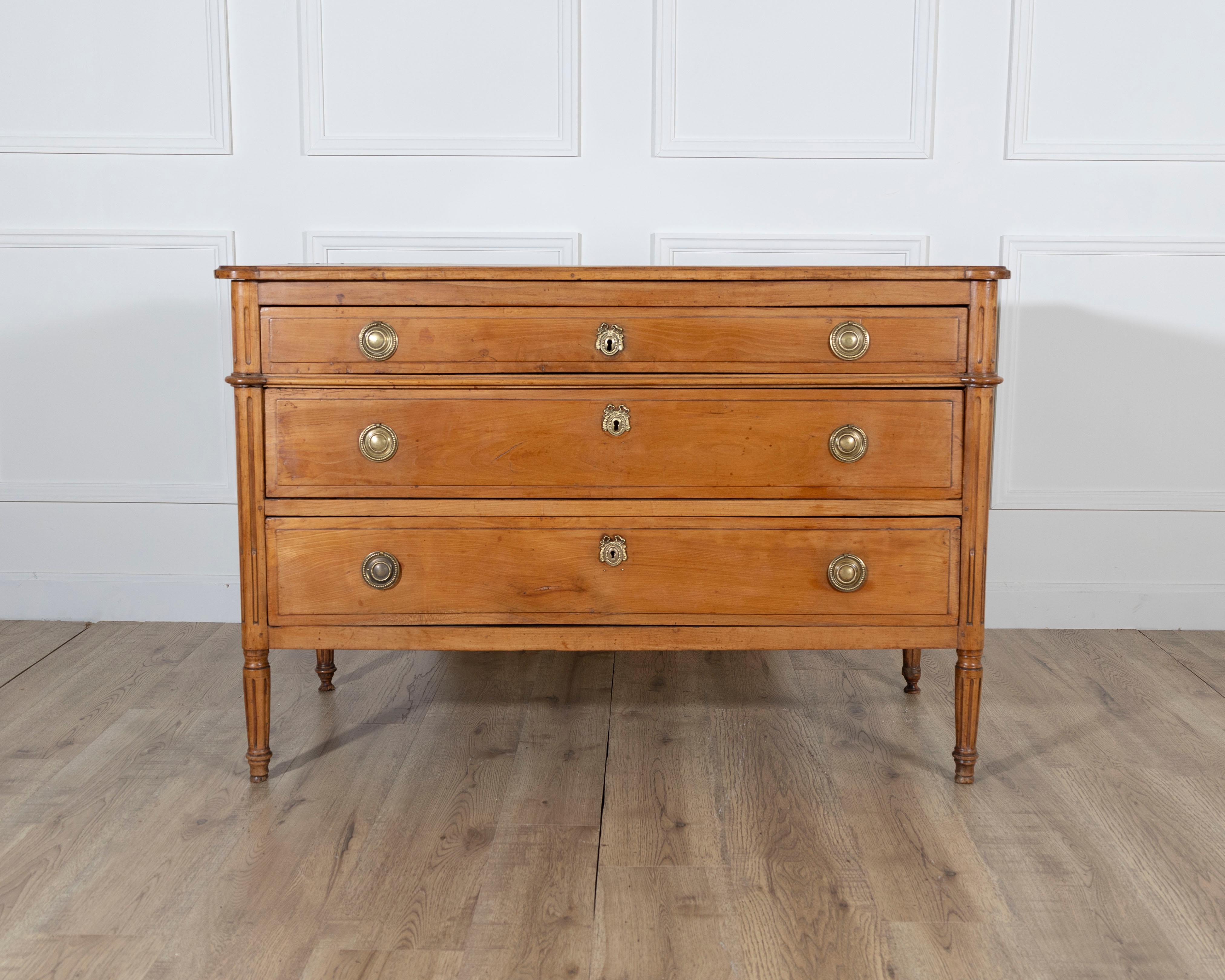 A stately Louis XVI period chest of drawers crafted in cherry wood, likely of Swiss origin, dating from the late 18th century. This elegant commode features three full-length drawers, each framed by fine crosspieces and adorned with classic circular