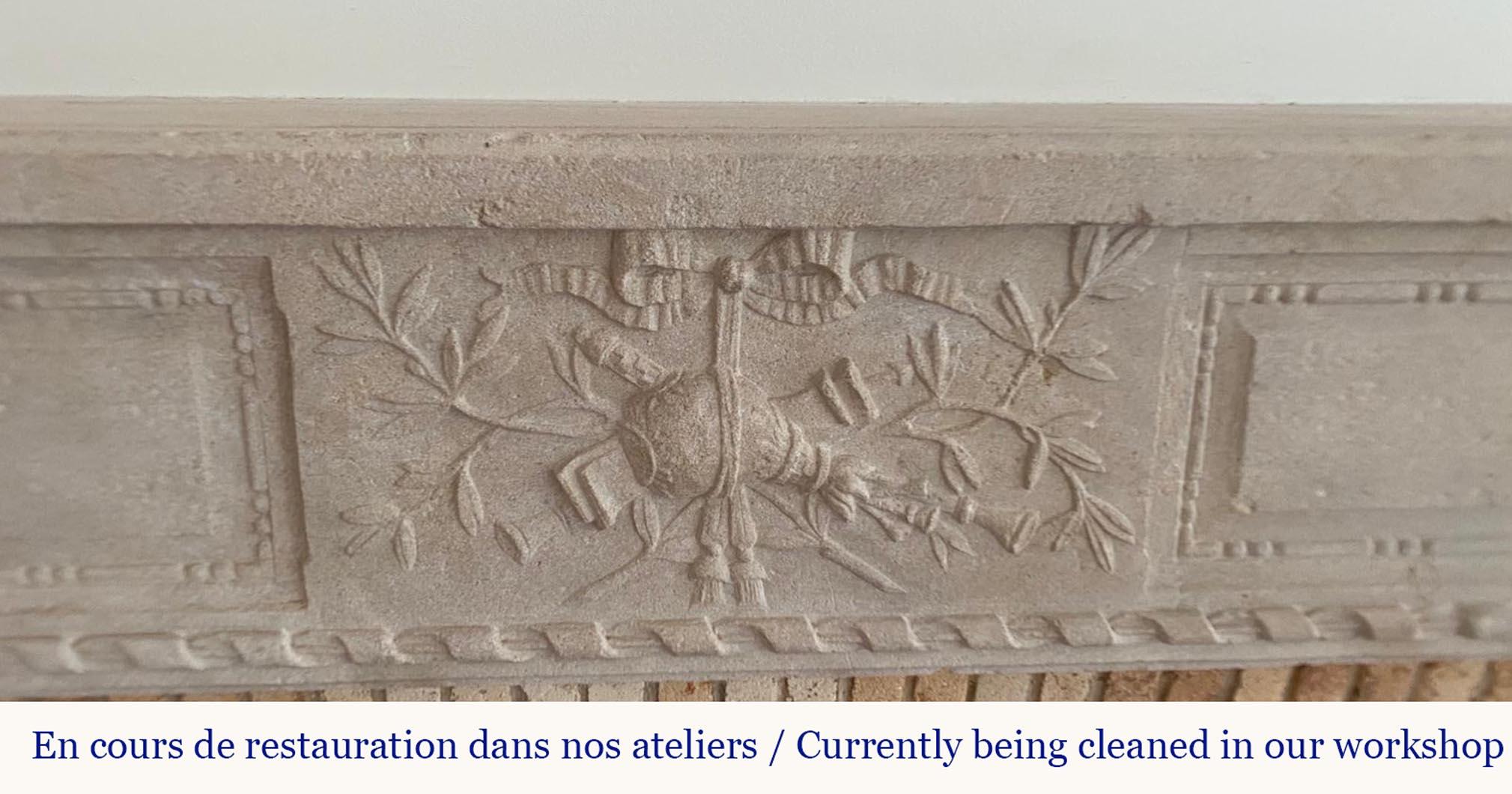 This elegant Louis XVI period fireplace, crafted from stone, features the refined neoclassical ornamentation characteristic of the late 18th century. The central frieze is adorned with a finely sculpted trophy motif—a quiver, flutes, and laurel