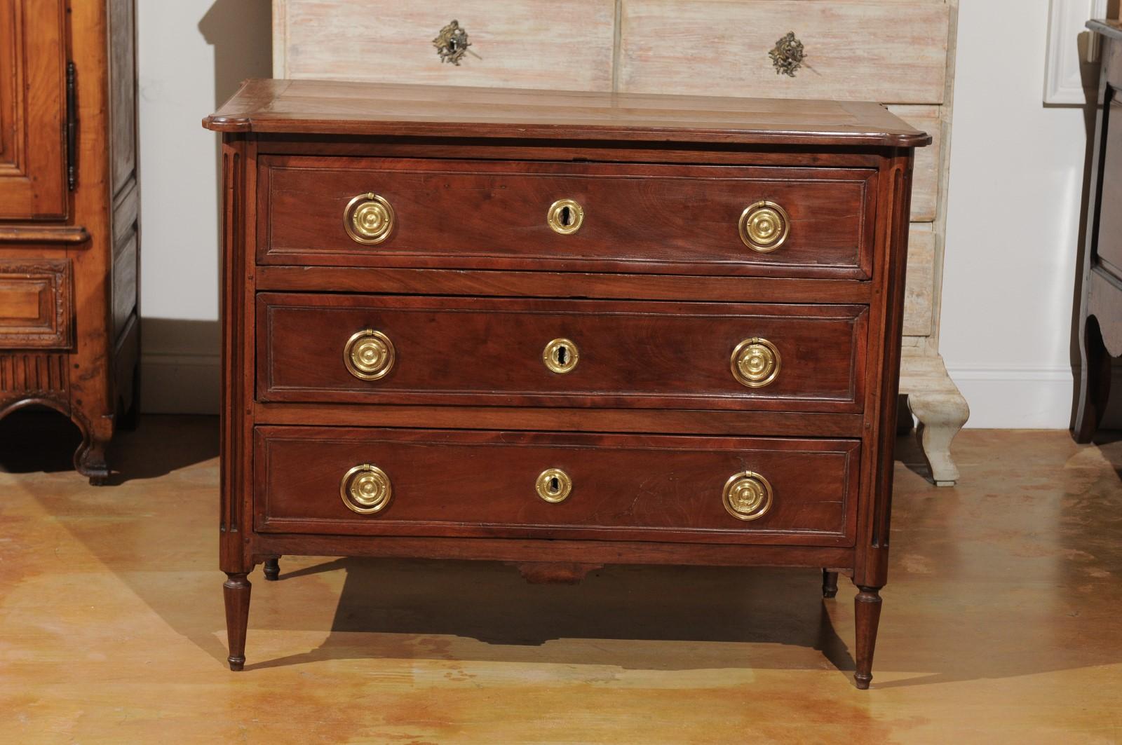 A French Louis XVI period walnut three-drawer commode from the last quarter of the 18th century, with original bronze and brass hardware, banded drawers and fluted legs. Born under the reign of the last monarch of the Ancien Régime, this French