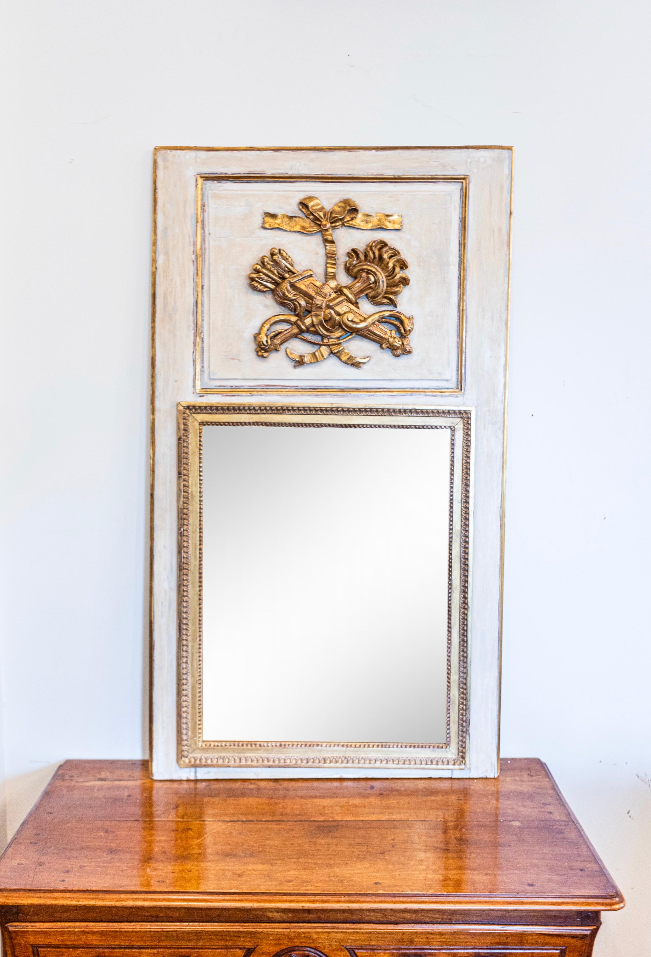 A French Louis XVI period gray painted and gilded trumeau mirror from circa 1790 with carved torch and quiver motif. This exquisite French Louis XVI period trumeau mirror, dating back to circa 1790, is a masterpiece of classic design and romantic