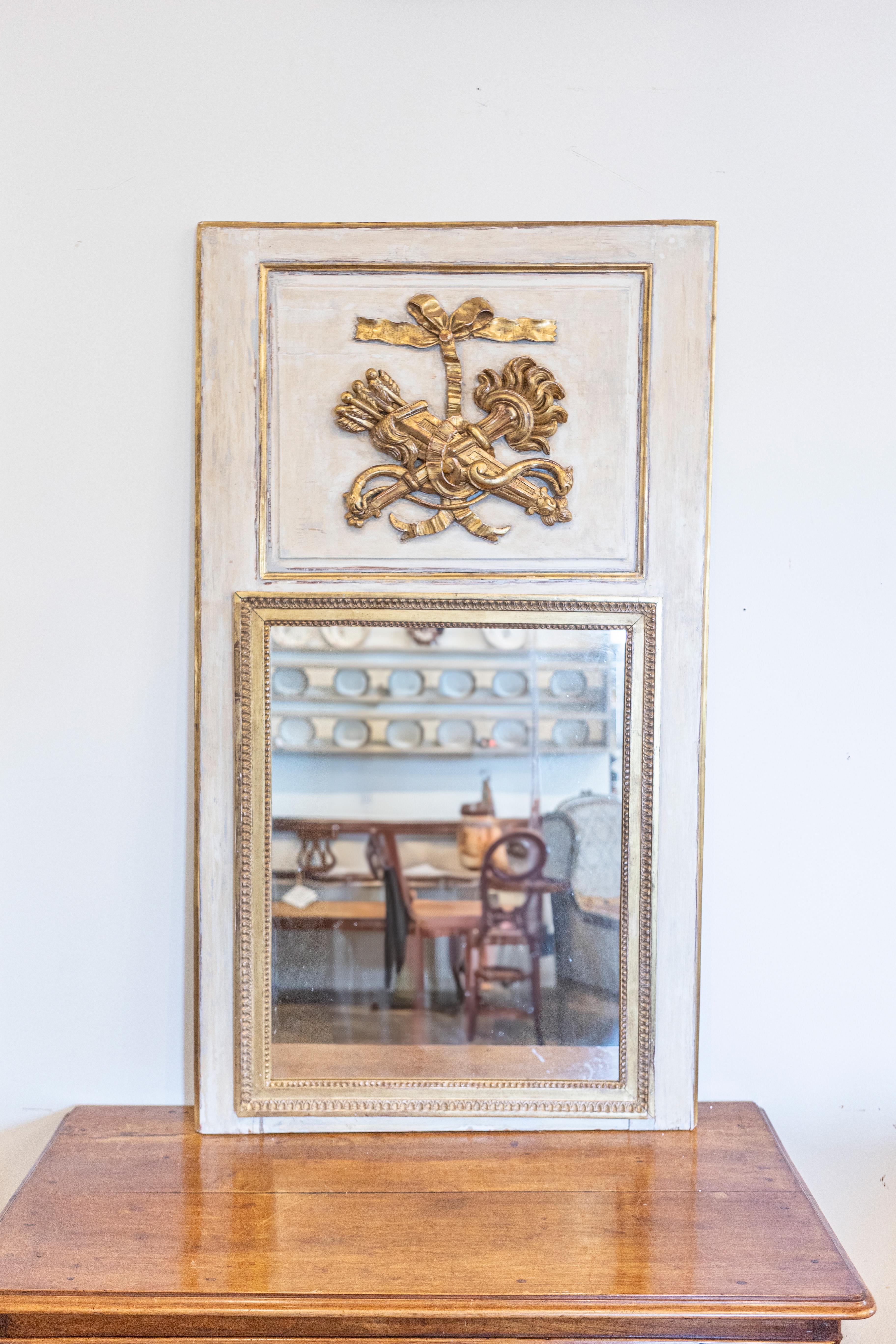 A French Louis XVI period gray painted and gilded trumeau mirror from circa 1790 with carved torch and quiver motif. This exquisite French Louis XVI period trumeau mirror, dating back to circa 1790, is a masterpiece of classic design and romantic