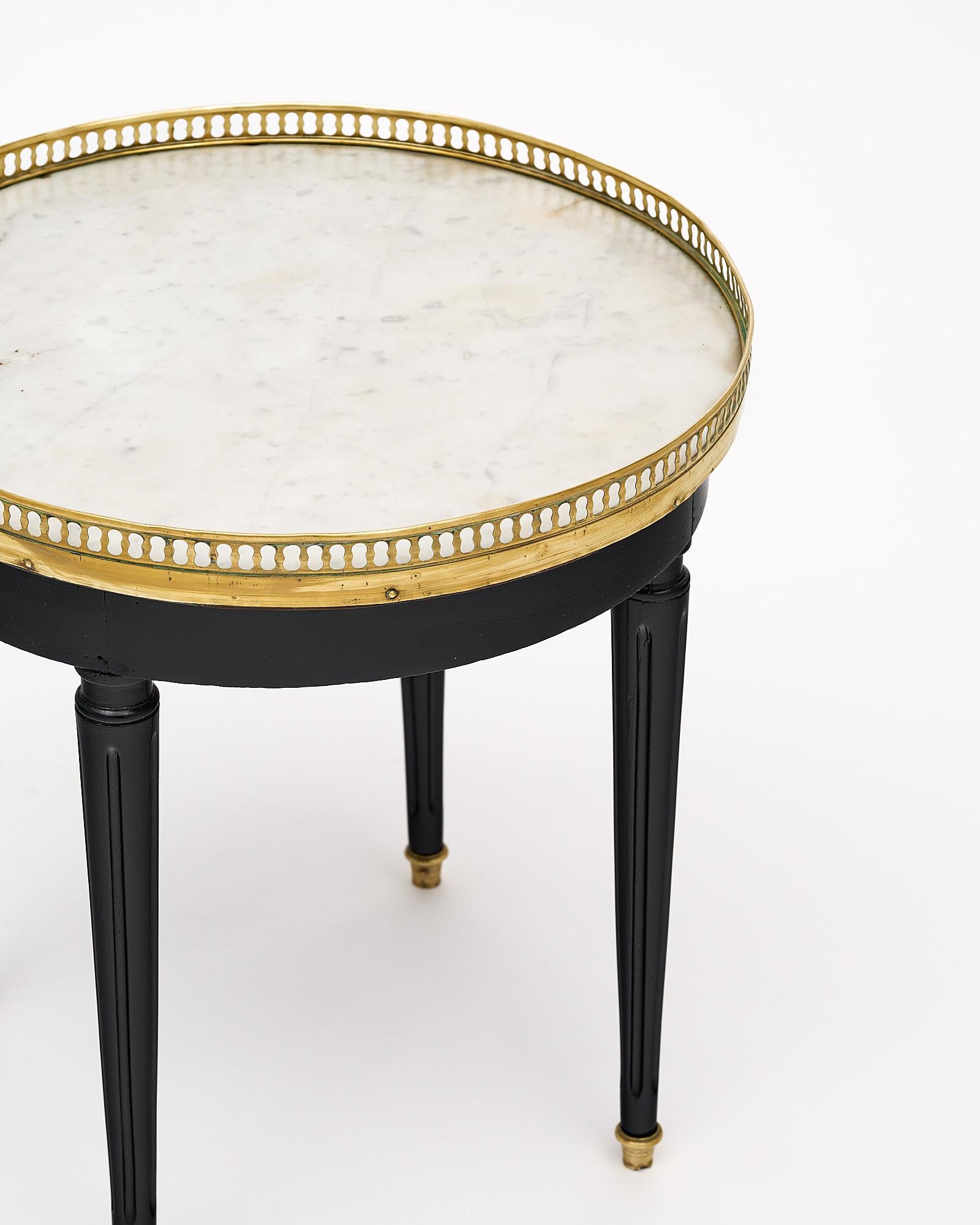 Side table, French, in the Louis XVI style. This petite “bouillotte” table is finished in an ebony lustrous French polish. The table features a Carrara marble top trimmed with an opened brass gallery and four tapered and fluted legs.
