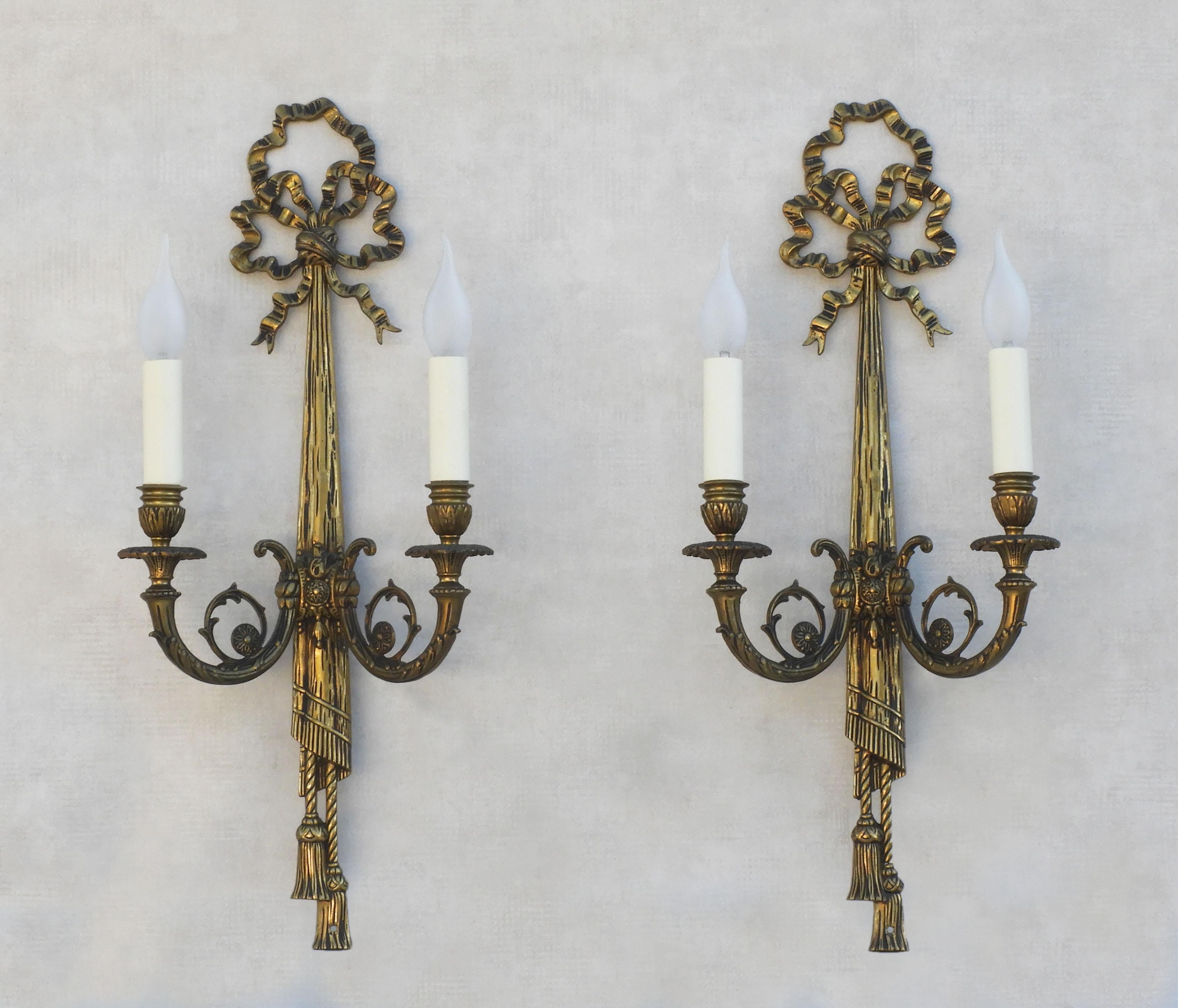 A large pair of French Louis XVI revival bow and tassel wall light sconces. Twin-armed ‘grand appliqués’ in cast bronze with elaborately decorated arms and chased detailing, each with two 'faux' candlelights. In great vintage condition with good