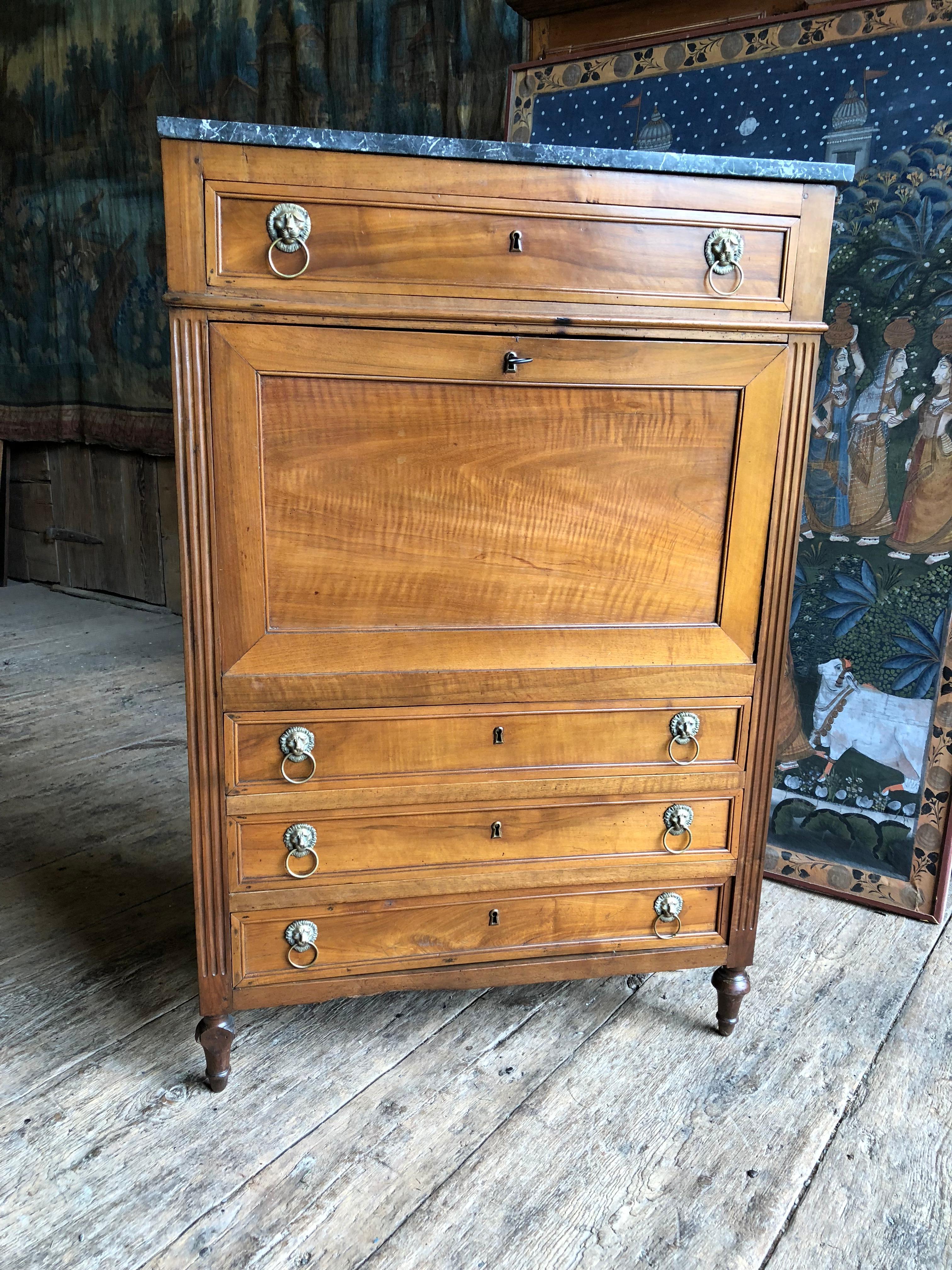A nice Louis XVI drop-front secretaire desk in blonde walnut, circa 1790, with its original grey marble top, brass lion’s head drawer pulls and working lock and key. The interior is fitted with small drawers and shelves and retains its original