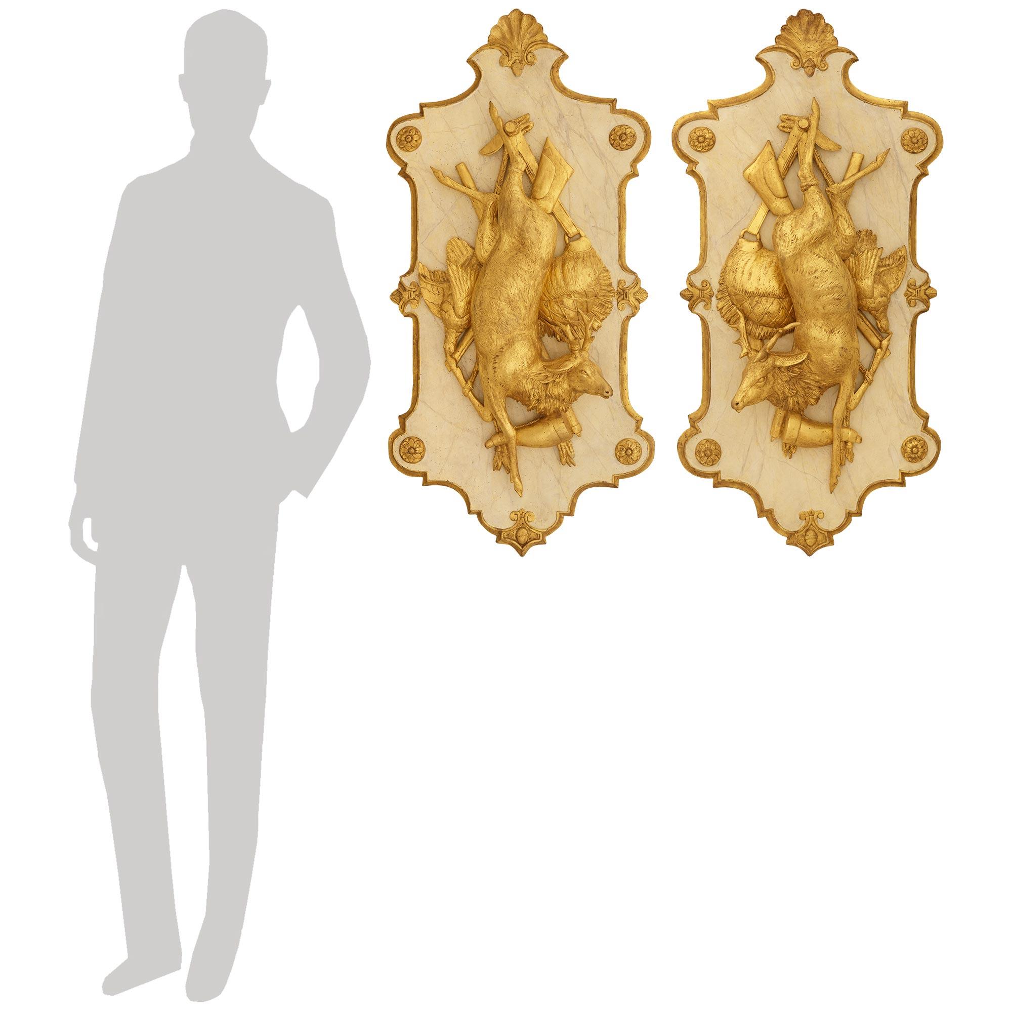 Paire de plaques en bois doré et en faux marbre peint de haute qualité et extrêmement décoratives, datant du milieu du XIXe siècle et de style Louis XVI. Chaque plaque de style trophée de chasse représente au centre un cerf merveilleusement sculpté