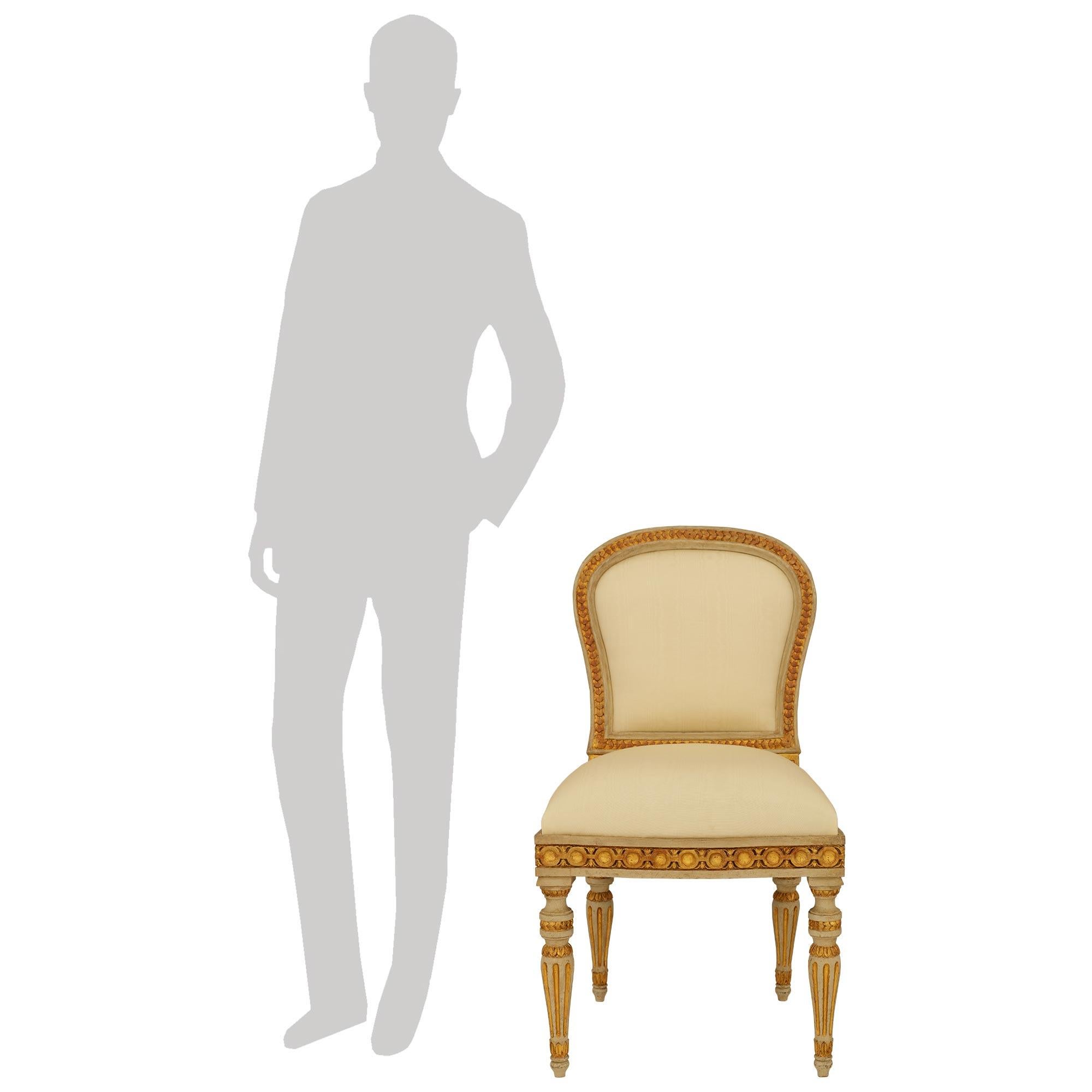 An elegant and complete set of ten Italian mid 19th century Louis XVI st. patinated Wood and Giltwood 'A Chassis' dining chairs. Each wonderful chair is raised by circular greyish blue patinated tapered and fluted legs with Giltwood flutes above