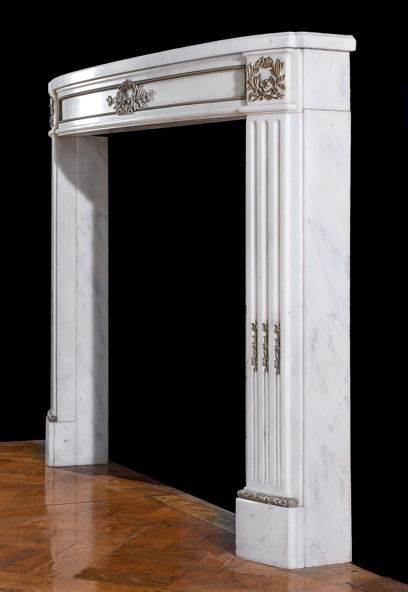A small finely carved statuary marble Louis XVI antique chimneypiece with a gently curved bow fronted shelf and frieze adorned with applied ormolu ornamentation in the form of laurel wreaths to the frieze, endblocks and the stop fluted jambs.