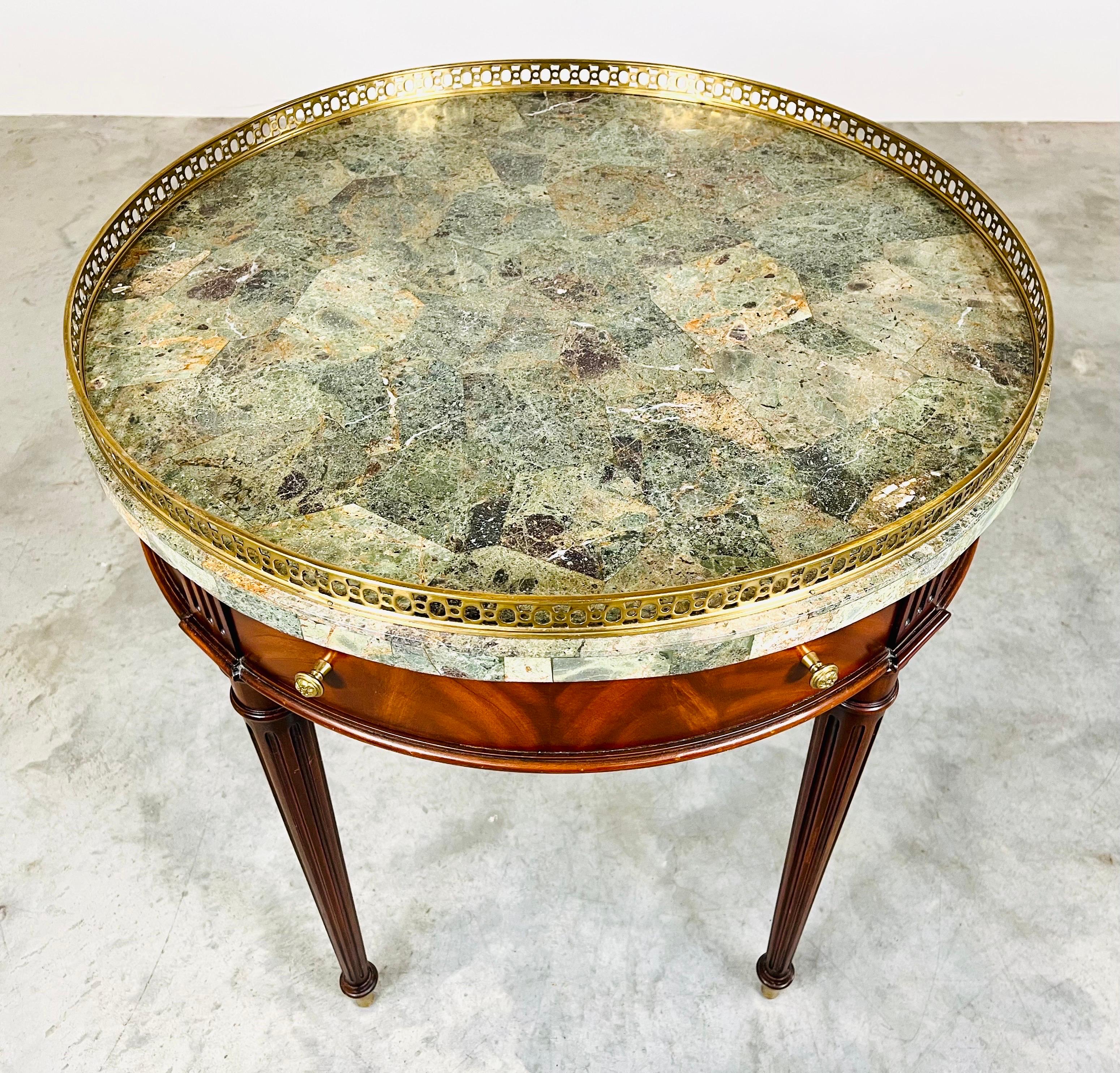 Louis XVI style round bouillotte table having hand-carved mahogany frame, verde green marble top adorned with a brass gallery. Features 2 opposed drawers for storage. Absolutely stunning in person. Very elegant and in beautiful condition.