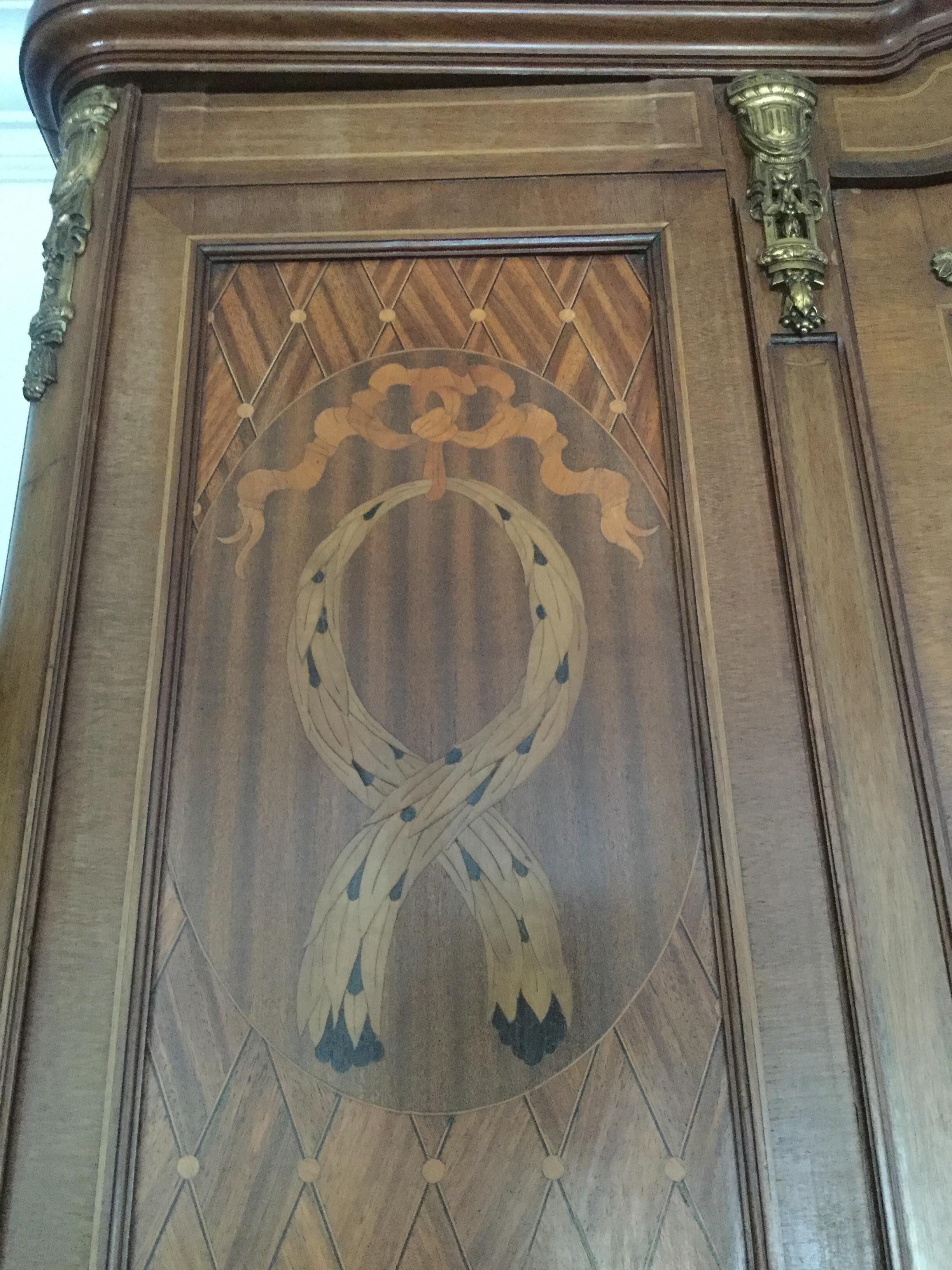 Handsome Louis XVI style walnut armoire. This 3-door armoire features a central beveled mirrored door and 2 side doors with marquetry. There is an hermine motif on each door made of inlaid wood and reminiscent of French royalty There are decorative