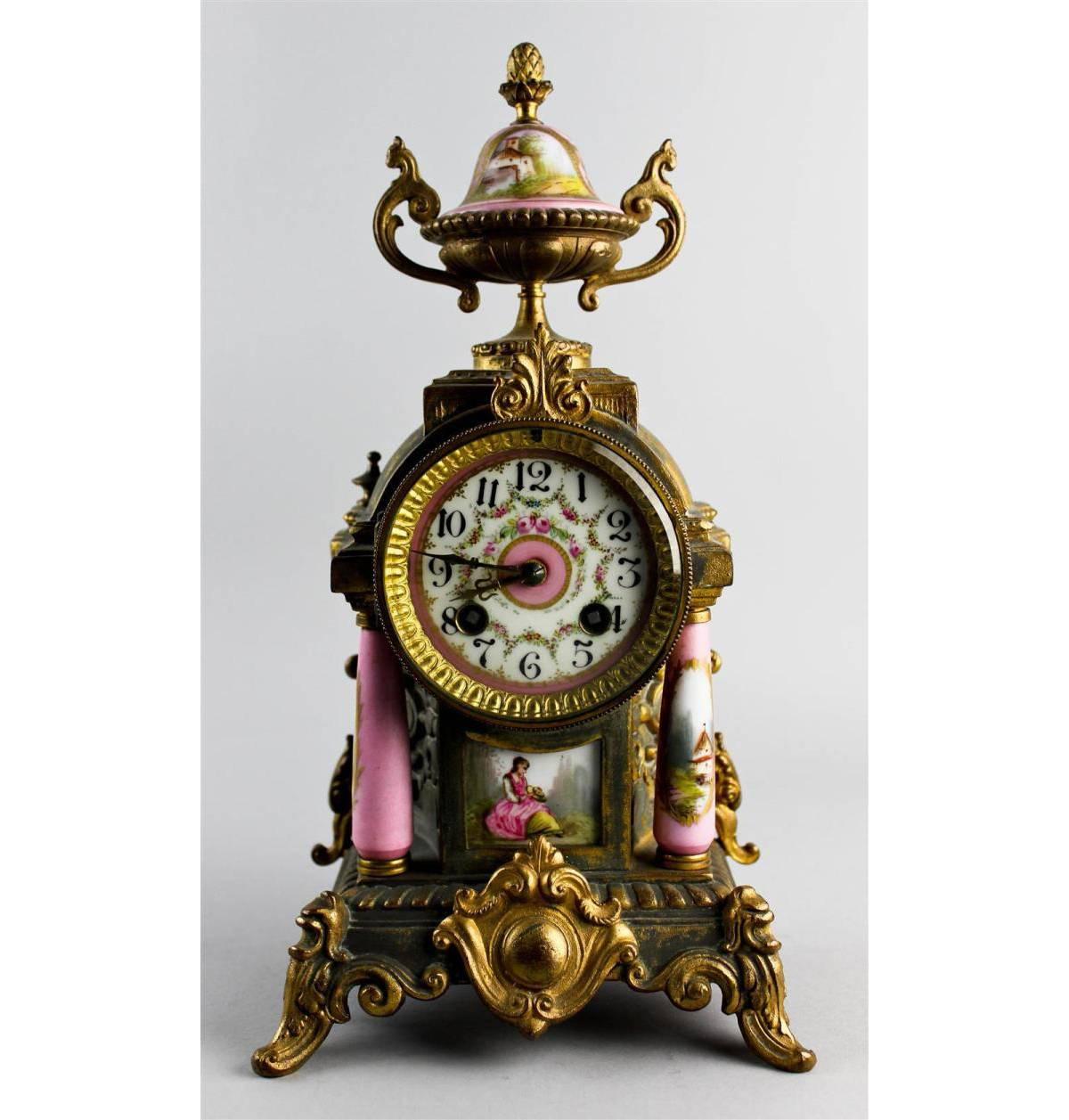 Early 20th century, the clock having a two train movement striking on a gong, with floral decorated enamel dial within an architectural housing with pink ground Sevres-style columns and urn form finial; the pair of urns, both decorated with a river