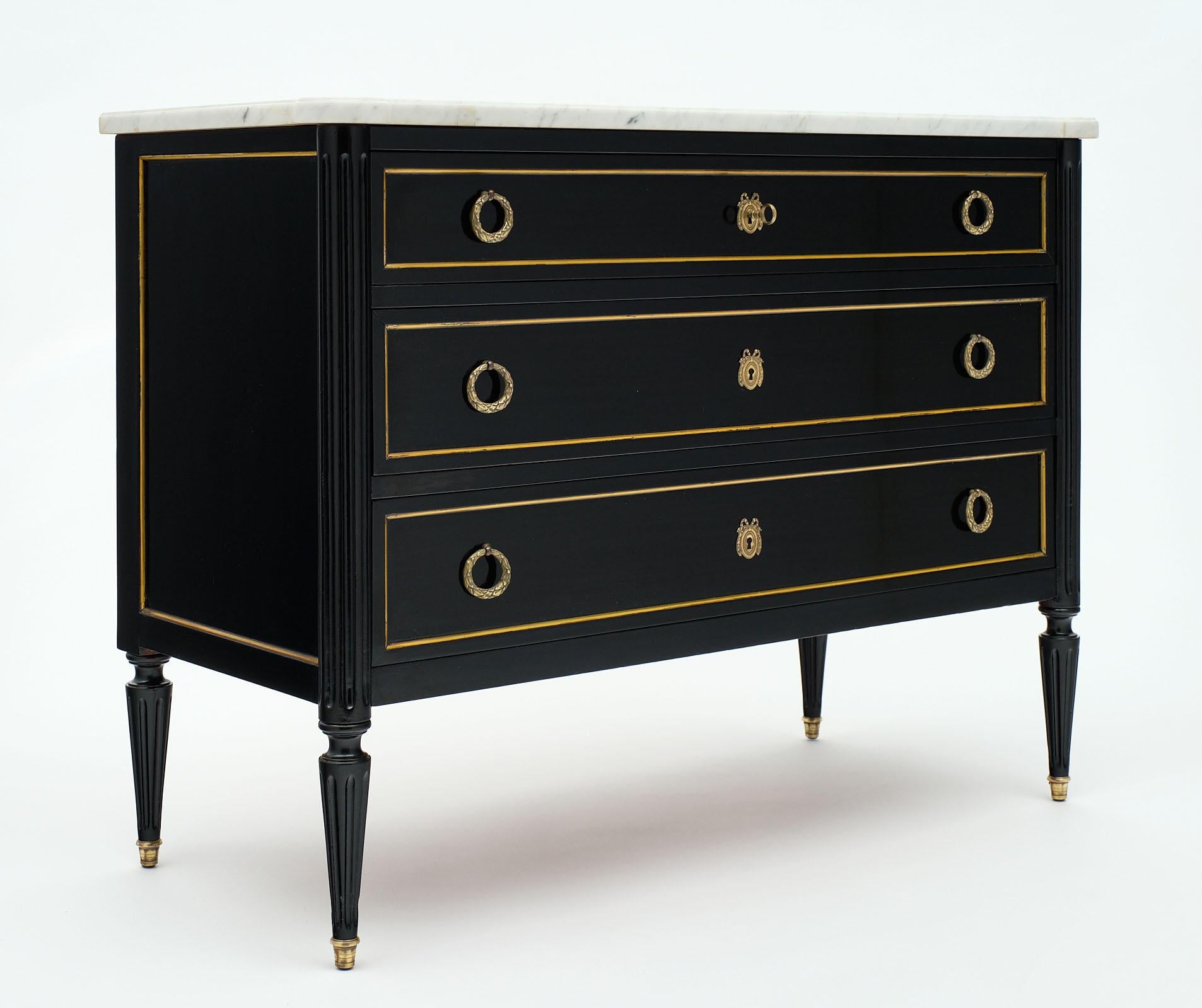 Louis XVI style antique chest of drawers made of mahogany and finished with an ebonized French polish for luster. The gilt brass trims and hardware throughout add an elegant touch. We love the tapered legs and proportions. There are three dovetailed