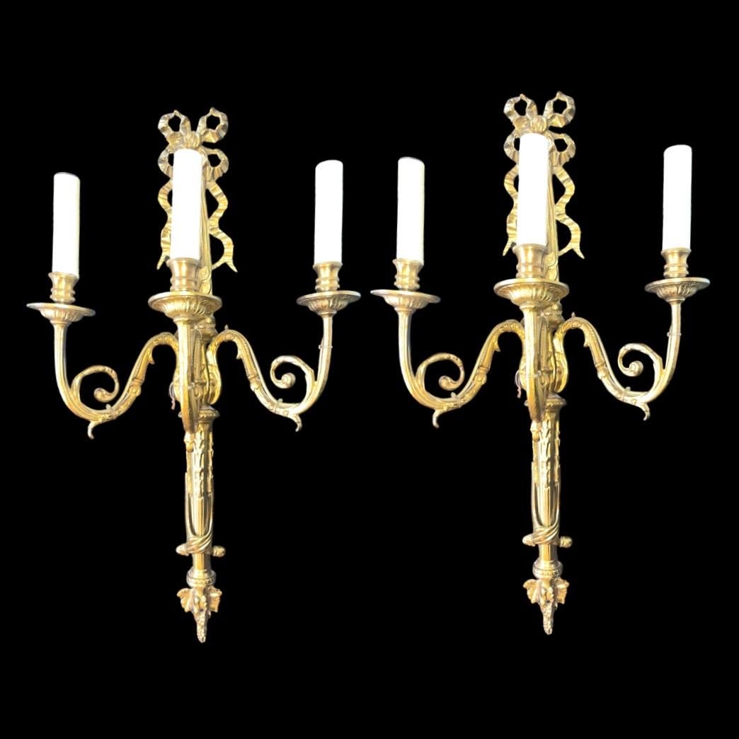 A captivating duo of brass wall lights, each adorned with three graceful arms and an exquisite ribbon crown detail. These splendid reproductions exude the timeless elegance of the Louis XVI style.

Crafted with meticulous attention, these wall