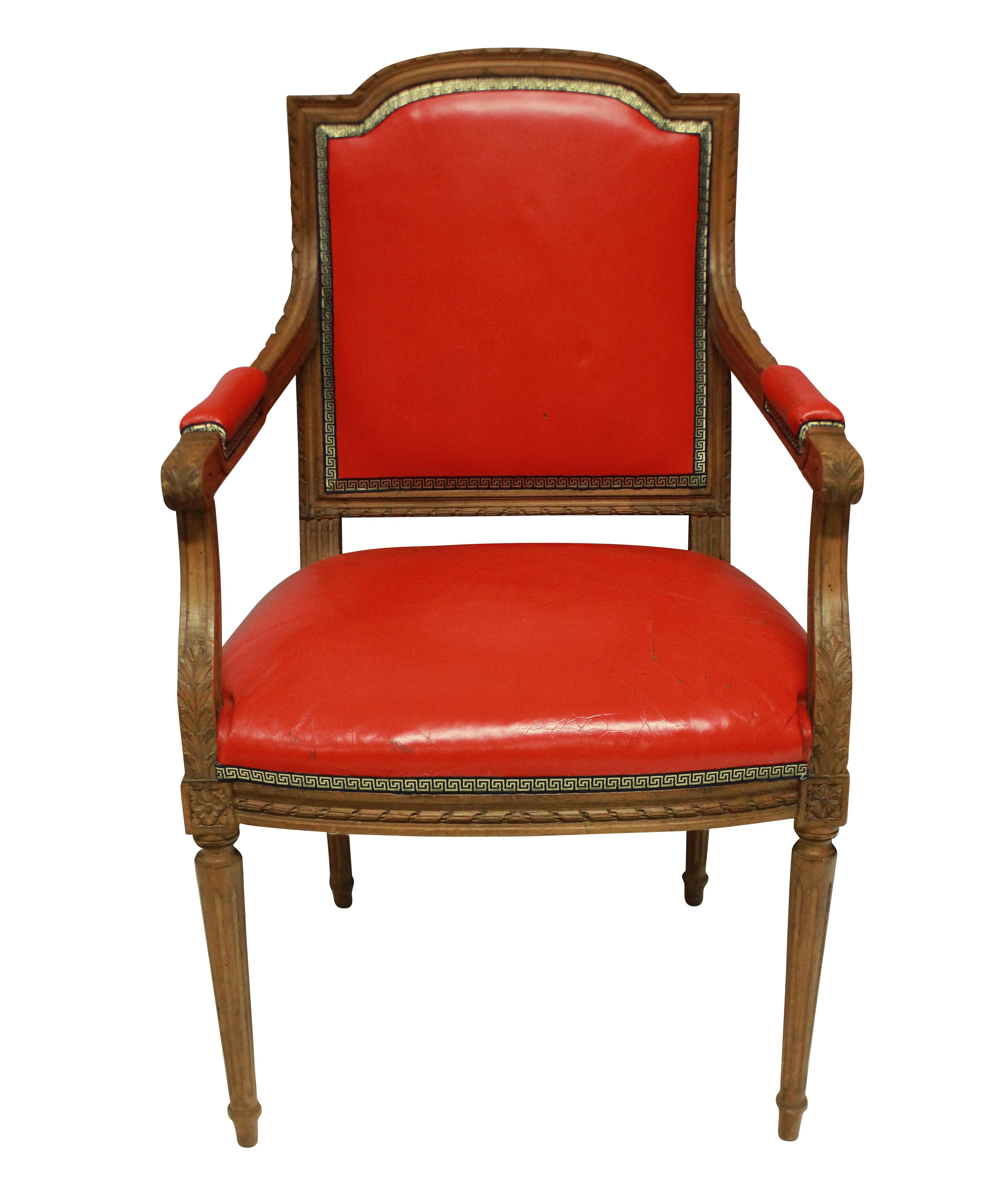 A Louis XVI style armchair in oak, upholstered in tomato red leather, with a blue and gold Greek key trim.