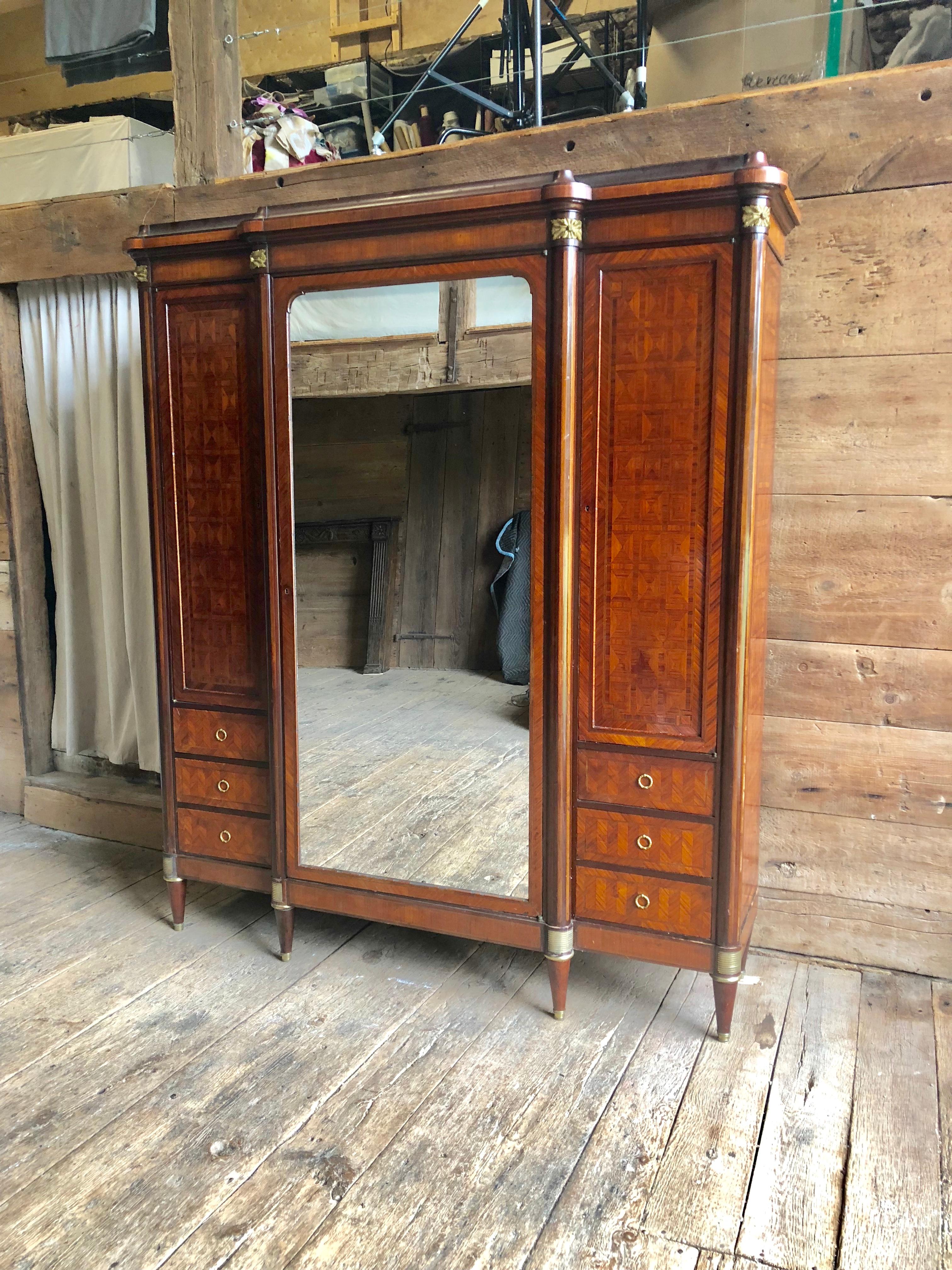 A French Belle Epoche period armoire in the Louis XVI style with marquetry inlay, gilt bronze mounts and a mirrored door. The interior side cabinets and central cabinet each have 4 adjustable shelves. The piece disassembles easily for moving and