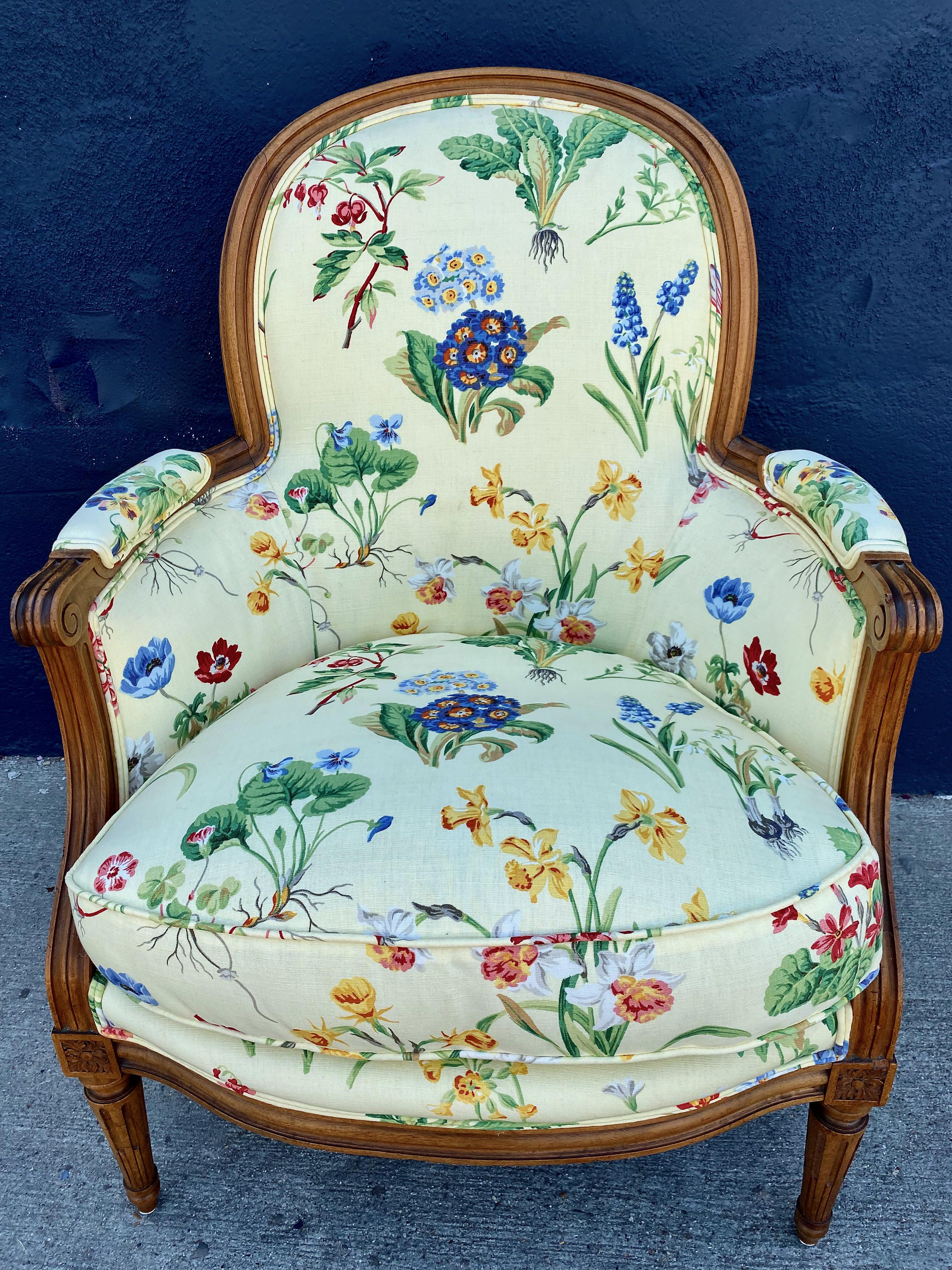 This is a charming late 19th century or early 20th century French walnut bergere that is upholstered in a vintage fabric with various flowers scattered on a pale yellow background. The walnut frame is well carved in. a Louis XVI style and is in