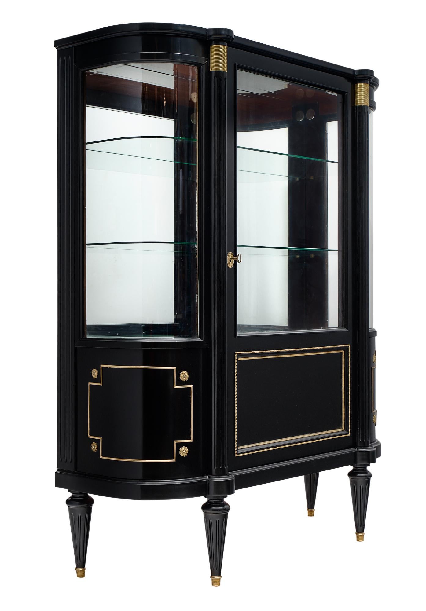 Louis XVI style bookcase from France made of mahogany that has been ebonized and finished with a museum-quality French polish. We love the curved glass shelves and brass trim throughout.