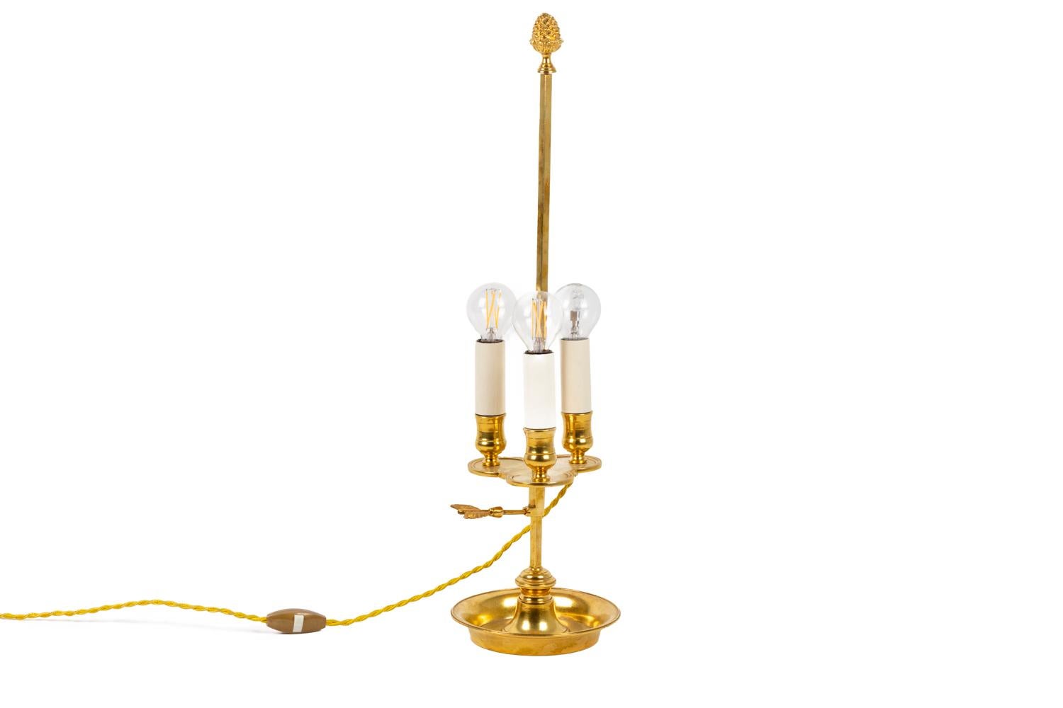 Bouillotte-Lampe im Louis XVI-Stil aus vergoldeter Bronze mit drei Lichtern. Der quadratische Schaft wird von einem Tannenzapfen gekrönt und ist mit einem Pfeil verziert. Eine dreiflügelige Oberfläche trägt die drei Lichter, deren Bögen mit