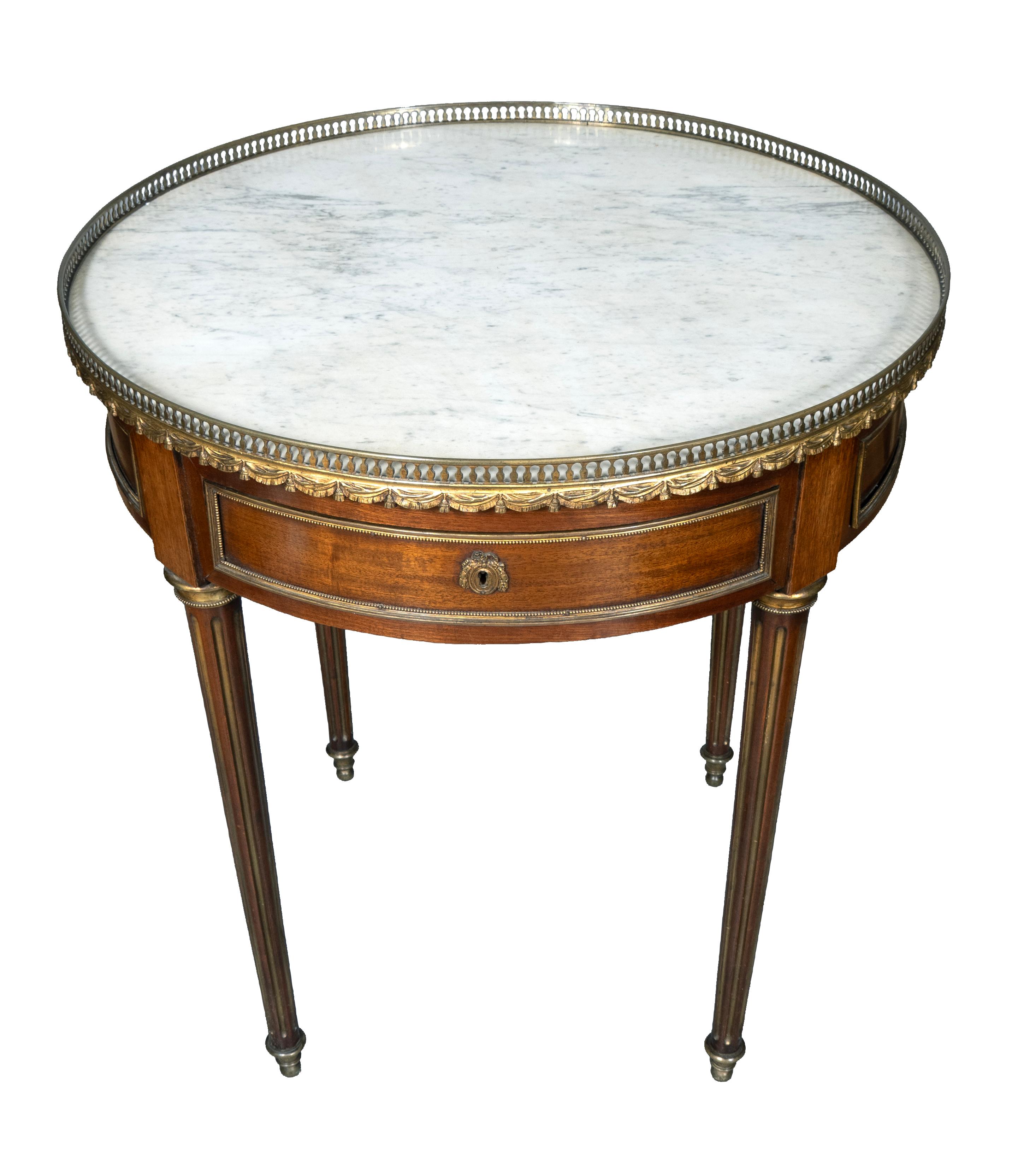 Un bel modello in ottime condizioni con piano rotondo in marmo bianco con galleria in ottone traforata su un fregio con un unico cassetto con serratura e chiave. Gambe circolari affusolate e scanalate con inserti in ottone. Piedi a sciabola.