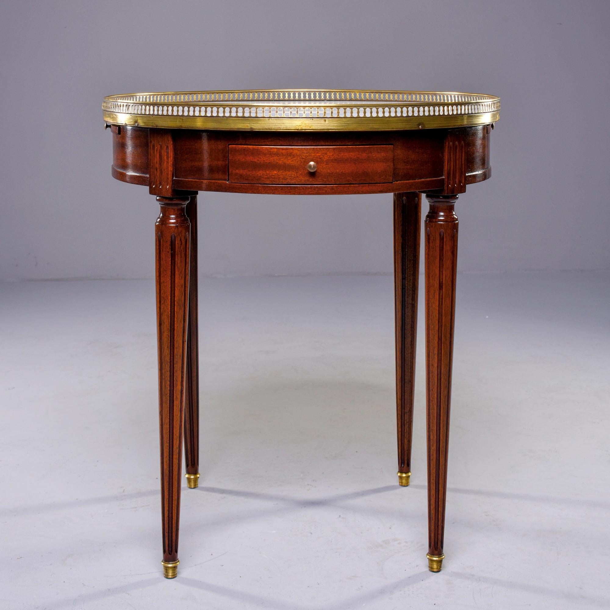 Circa 1900 French Louis XVI style Guéridon features a mahogany base with tapered, reeded and brass capped legs, a round white marble top with brass gallery and small drawer. Sides have leather covered extensions. Unknown maker. Classic and versatile