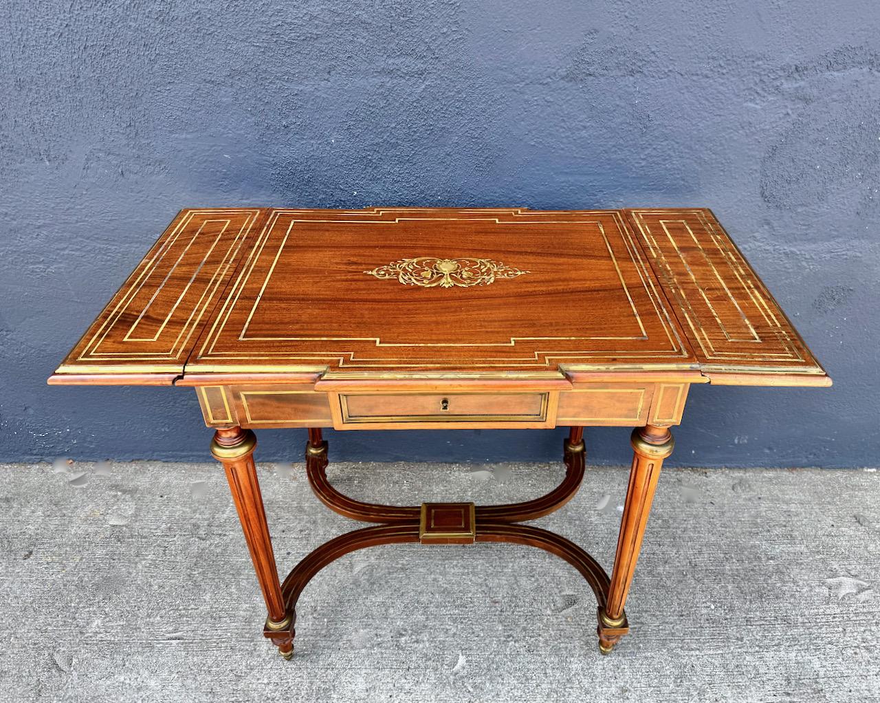 This is an outstanding example of a late 19th century late Louis XVI-style small writing table. Additionally, the table, with the drop leaves up, could serve as a sofa table. The beautifully figured mahogany veneer is detailed in fine brass string