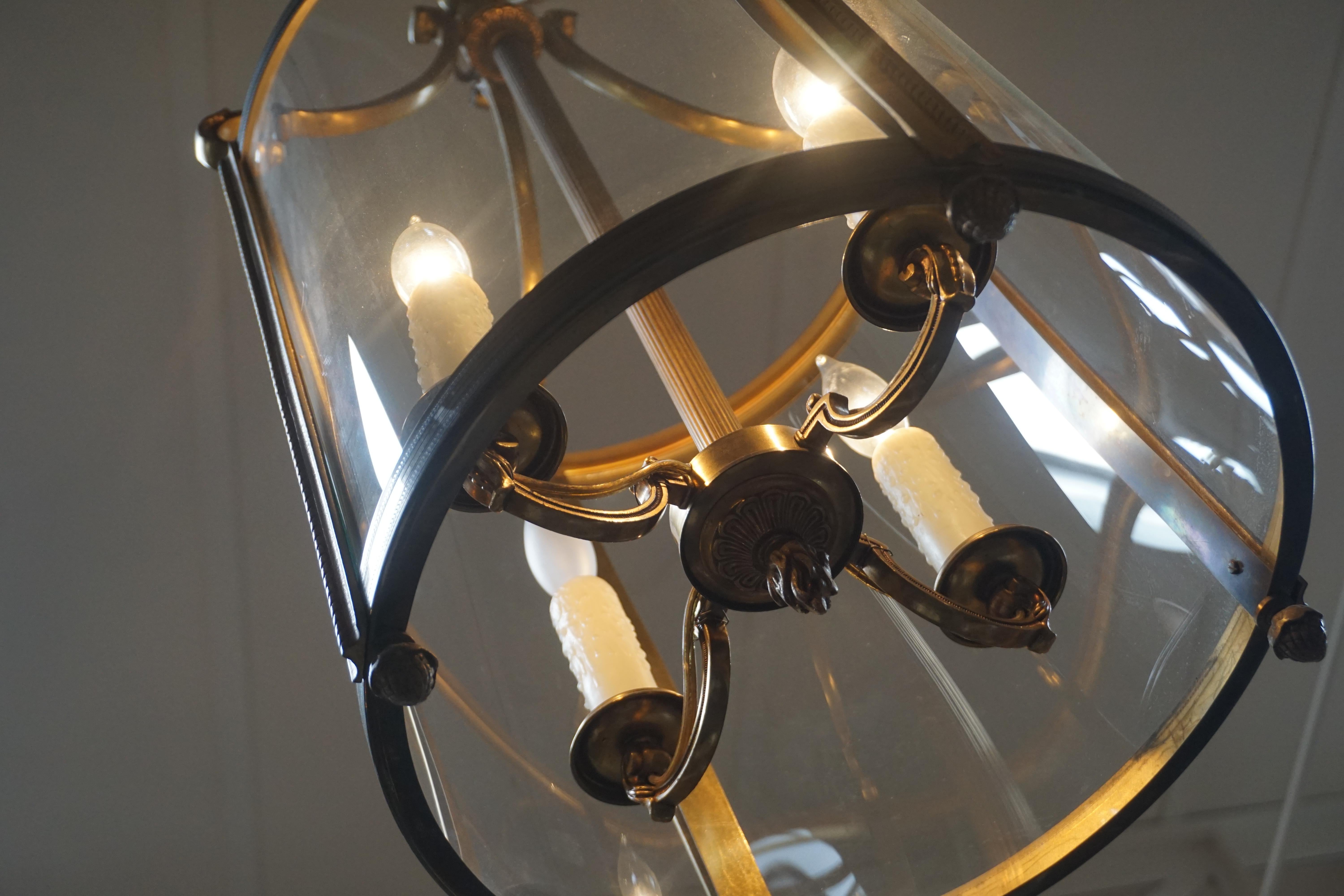Louis XVI style hanging brass lantern light fixture. Four serpentine arms attach below the double reverse scroll fixture loop from which the reeded tube of the four light chandelier is suspended. Each faux candle light rests in a simple round cup