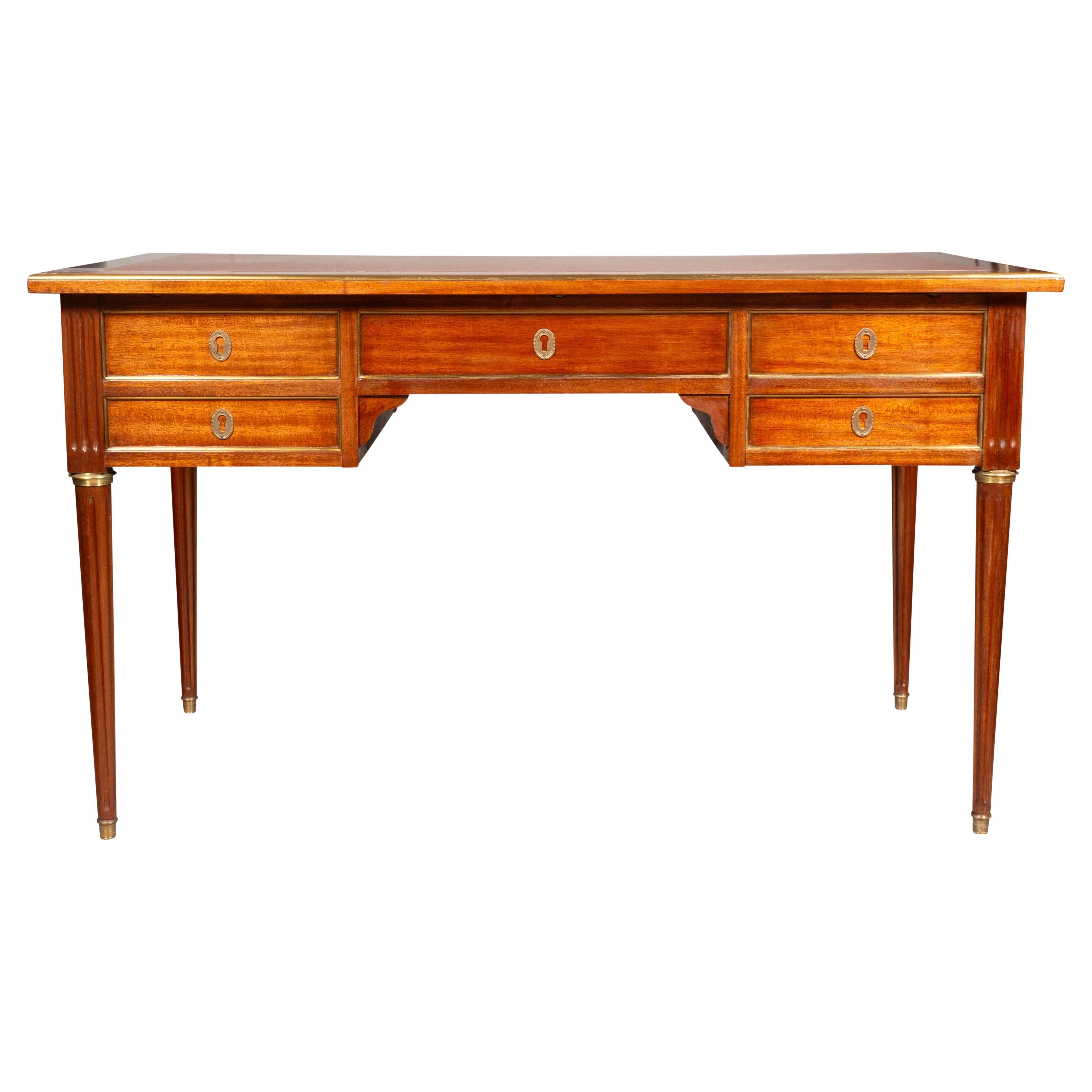 Rectangular top with inset brown leather over a central drawer flanked by a deep drawer and two single drawers. Finished on back with false drawers. Raised on circular tapered fluted legs and sabot feet.