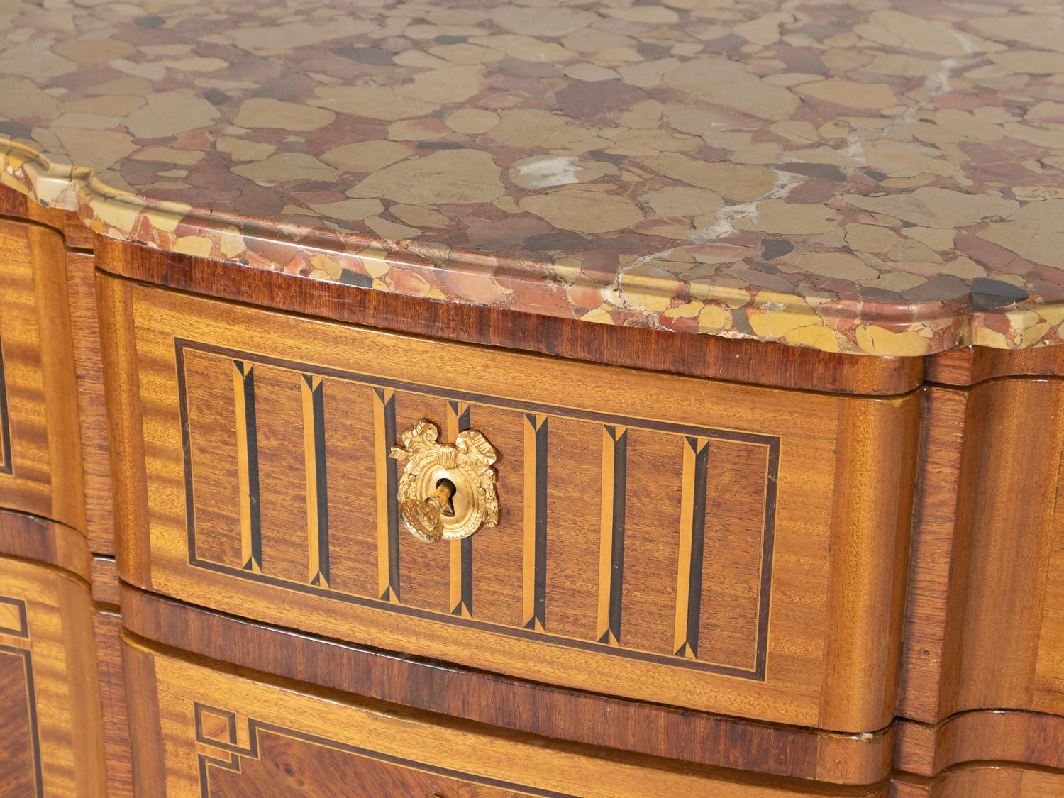 Piano in marmo a forma di fronte con bordo modanato, tre lunghi cassetti sagomati con pannelli impiallacciati in legno di tulipano e bordatura in ebano, cassetto superiore intarsiato con disegni in ebano e sicomoro. 
Maniglie a ghirlanda d'alloro in