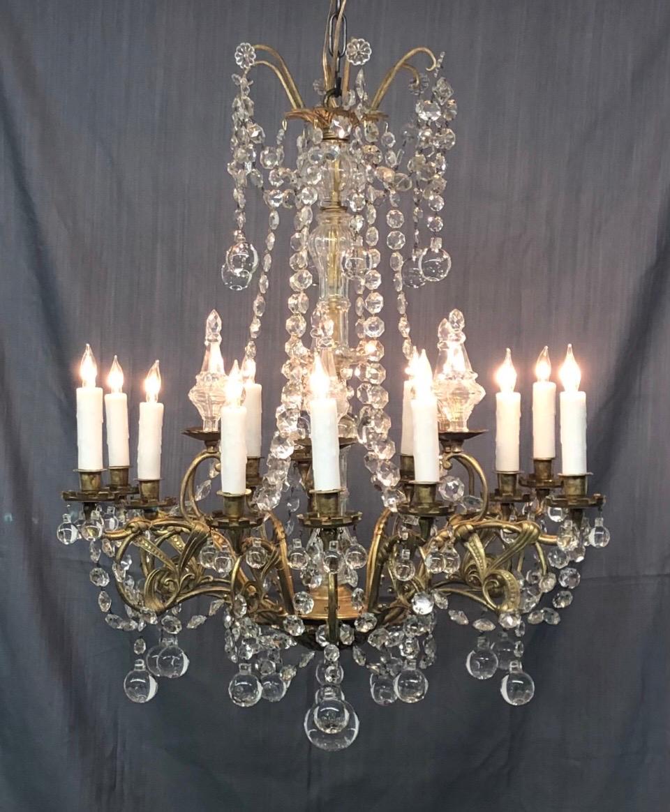 Elegant Louis XVI style Bronze Chandelier was originally candle and has since been rewired and electrified. The crown has six bronze scrolls with swaged crystal chains. The Crystal center column comes down to console holding twelve solid bronze