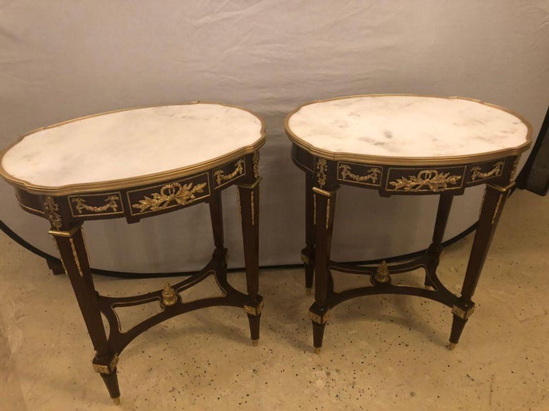 Louis XVI style doré bronze framed marble-top end or lamp tables with bronze mounts. The white Carrara marble top with grey veins supported by a set of tapering bronze fluted square legs each having an X-base undercarriage with a bronze finial in