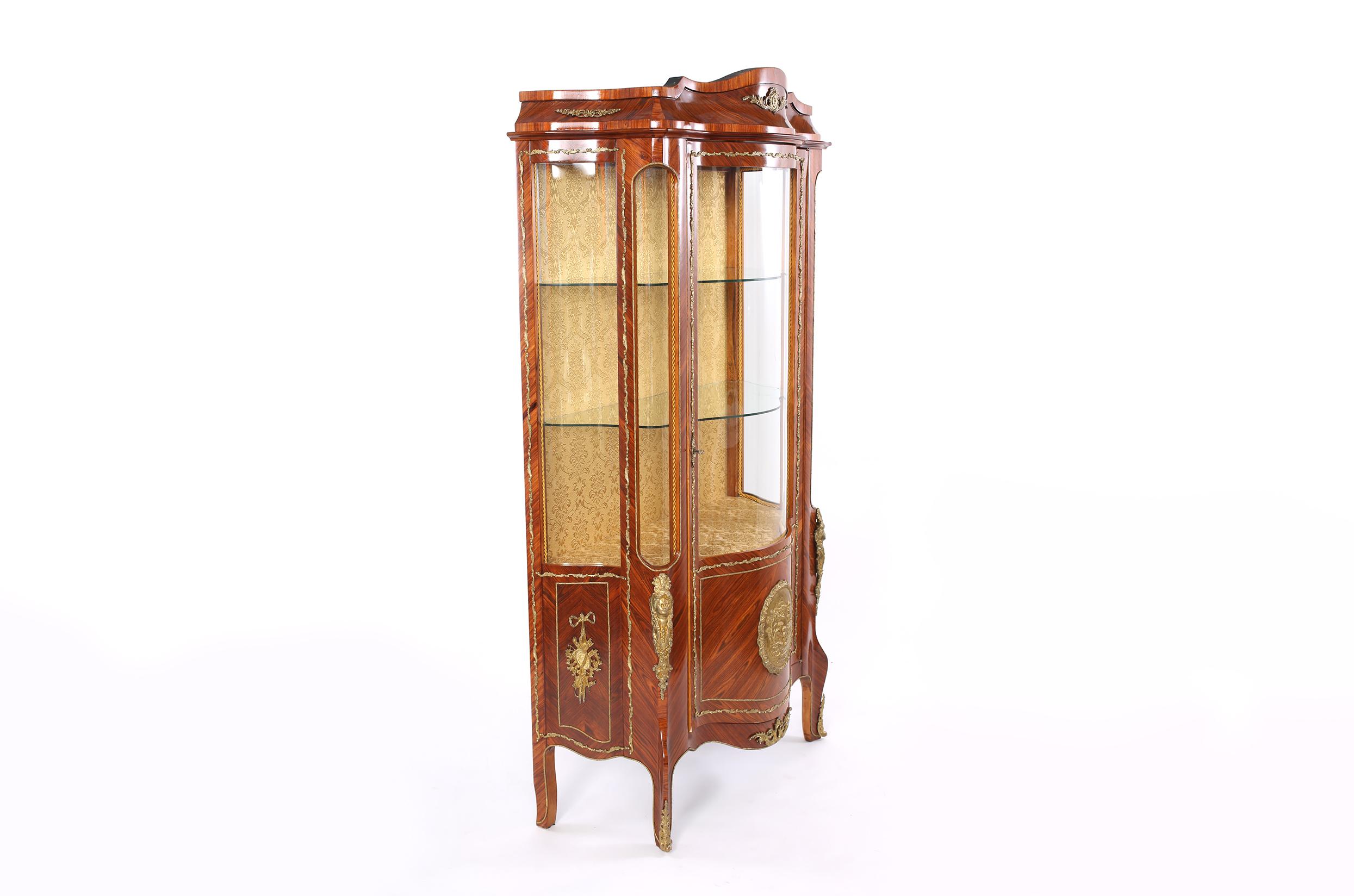 Louis XVI style with bronze mounted detail mahogany wood china display cabinet / vitrine with upholstered back interior design and glass shelves. The cabinet / vitrine is in good condition with age / use appropriate wear. The vitrine stand about 78