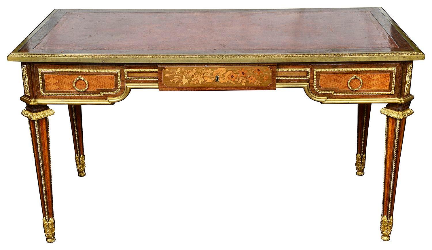 A very good quality late 19th Century French Louis XVI style bureau plat. Having an inset leather top, gilded ormolu mouldings and mounts. Trellis parquetry to the frieze, with floral inlaid marquetry panels to the four sides. Three frieze drawers,