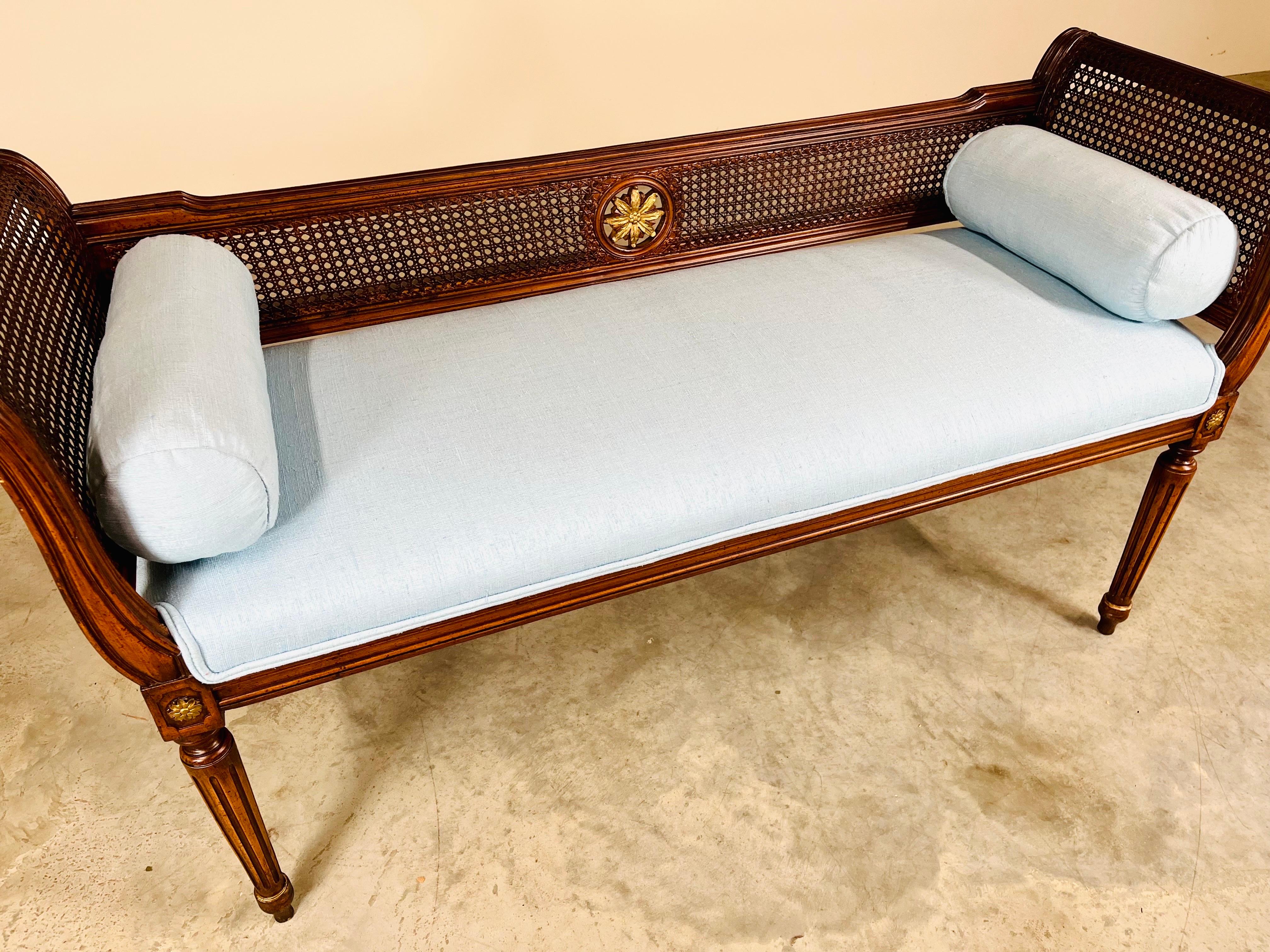 Louis XVI caned mahogany scroll arm window bench embellished with gold gilt rosettes, newly upholstered in new old stock blue silk with fresh cushioning. 
Excellent vintage condition having perfect cane throughout. Clean and ready for use!